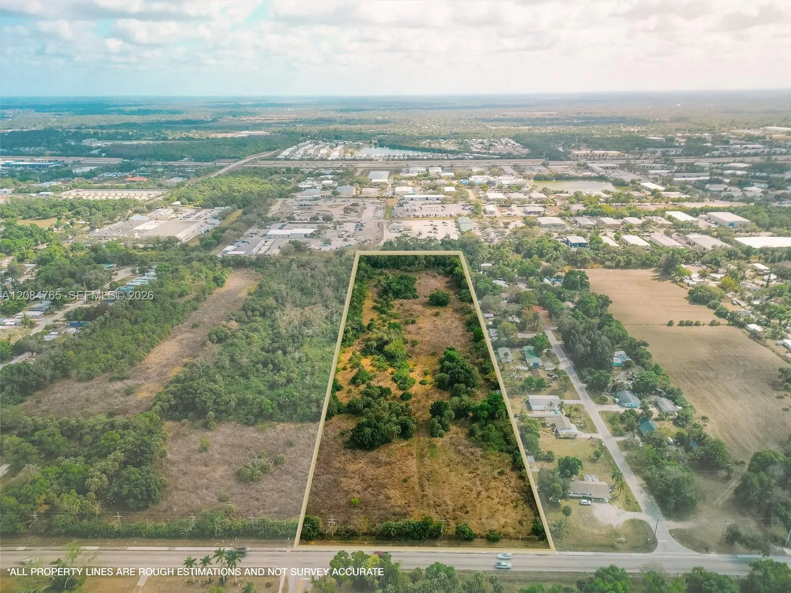 Stunning aerial drone view showcasing this vacant land parcel outlined amid mature trees, with easy paved road access and nearby residential development, a prime South Florida land investment opportunity.