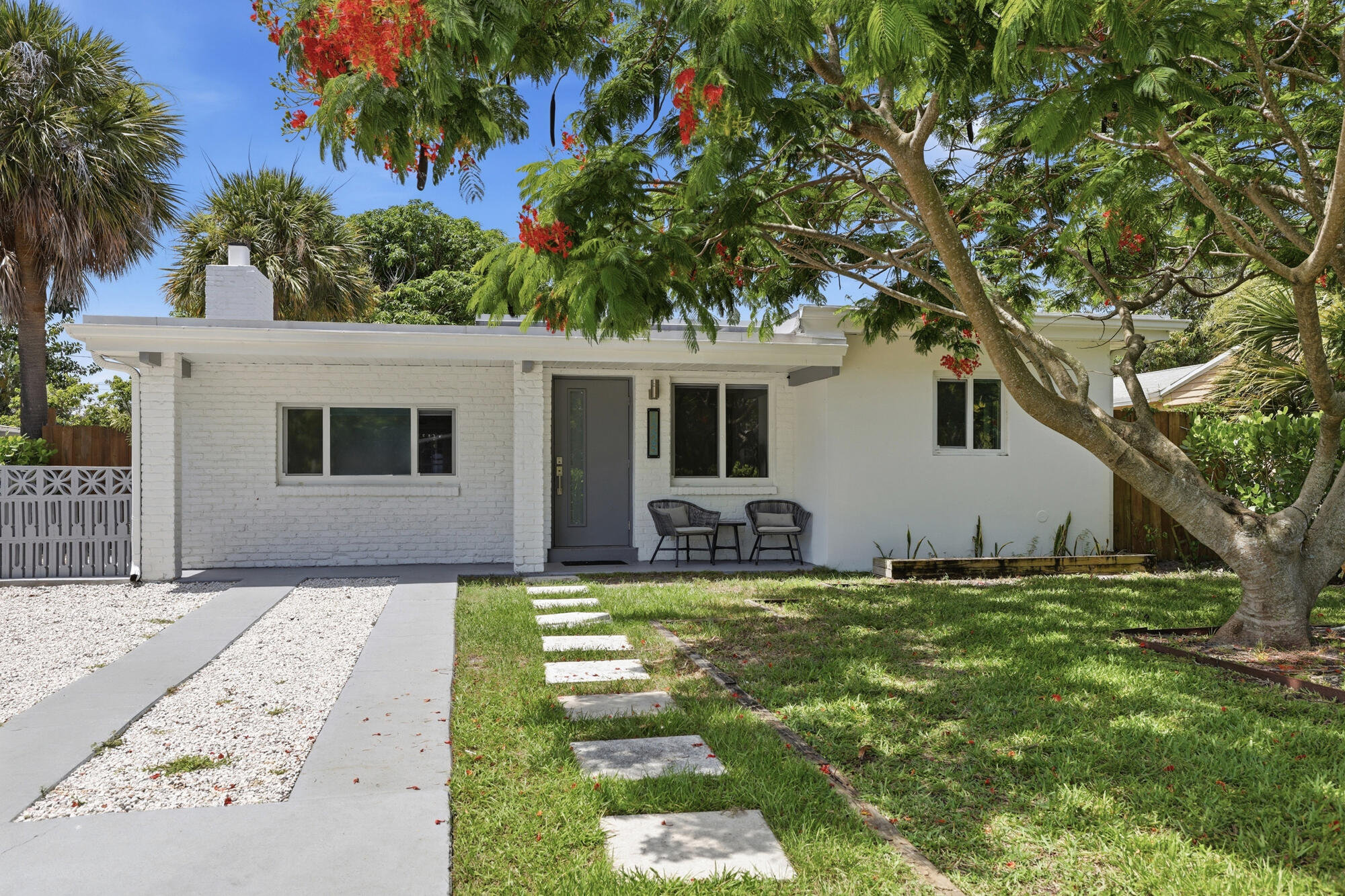 White brick and stucco exterior with a gray front door, flat roofline, and a driveway featuring concrete strips and white gravel