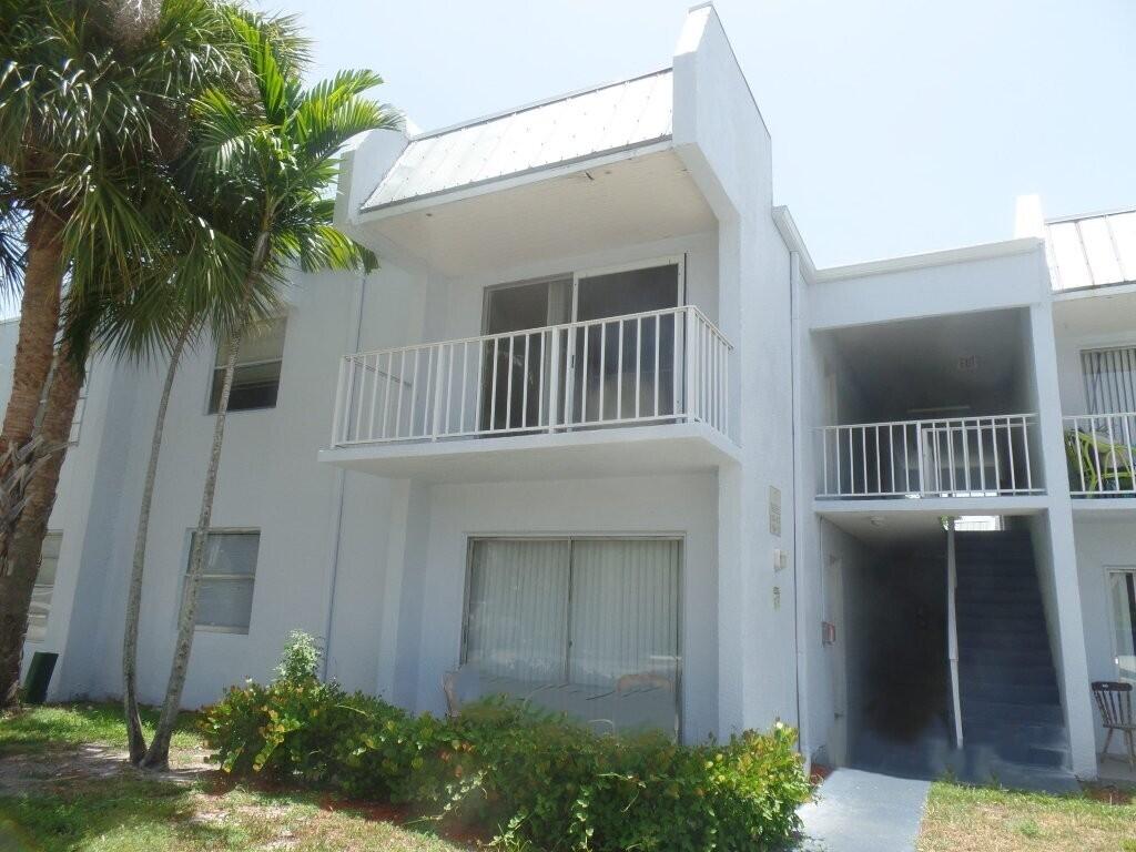 Multi-story stucco exterior featuring a second-floor balcony with white railings, sliding glass doors, and a metal roof