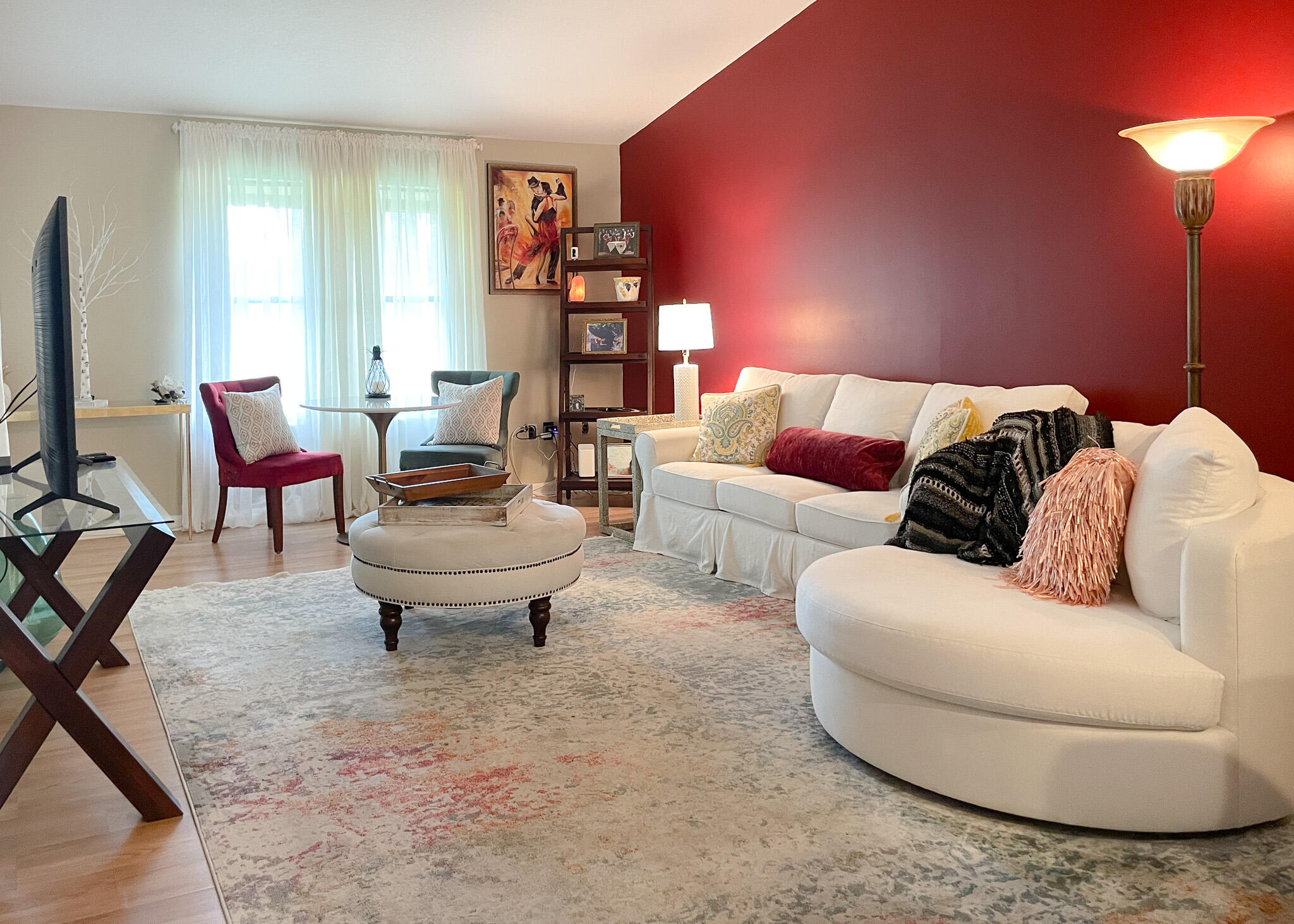 Living area featuring a prominent accent wall, wood-finish flooring, and multiple windows with sheer white curtains
