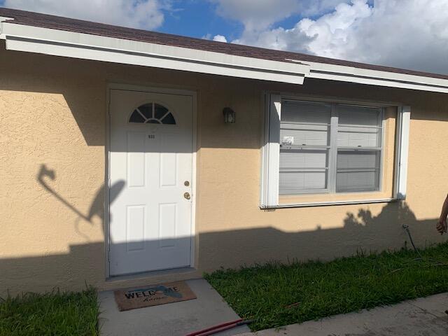 Stucco exterior featuring a white paneled entry door with an arched transom window and an exterior wall lantern