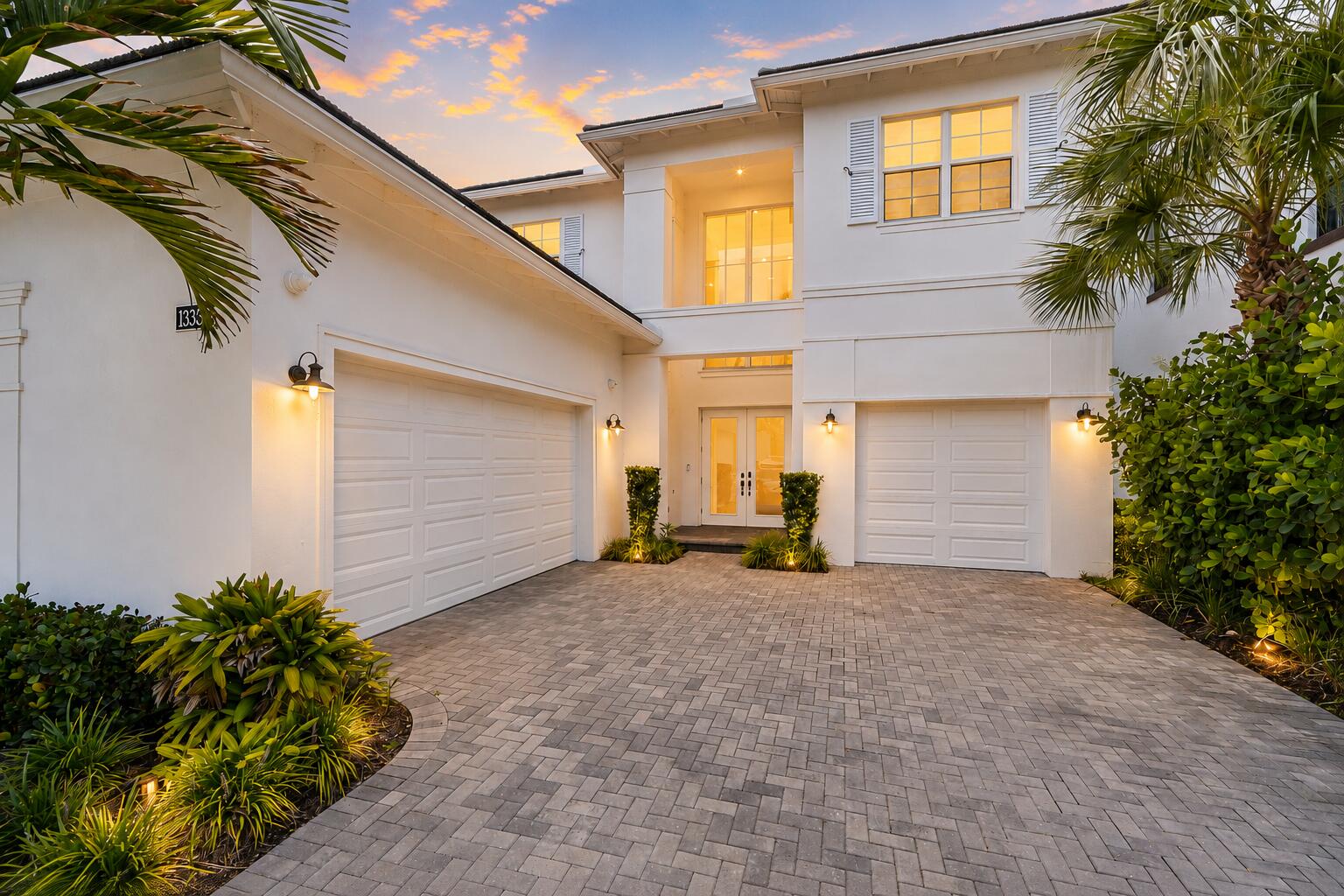 Two-story home exterior with three-car garage and paver driveway at dusk
