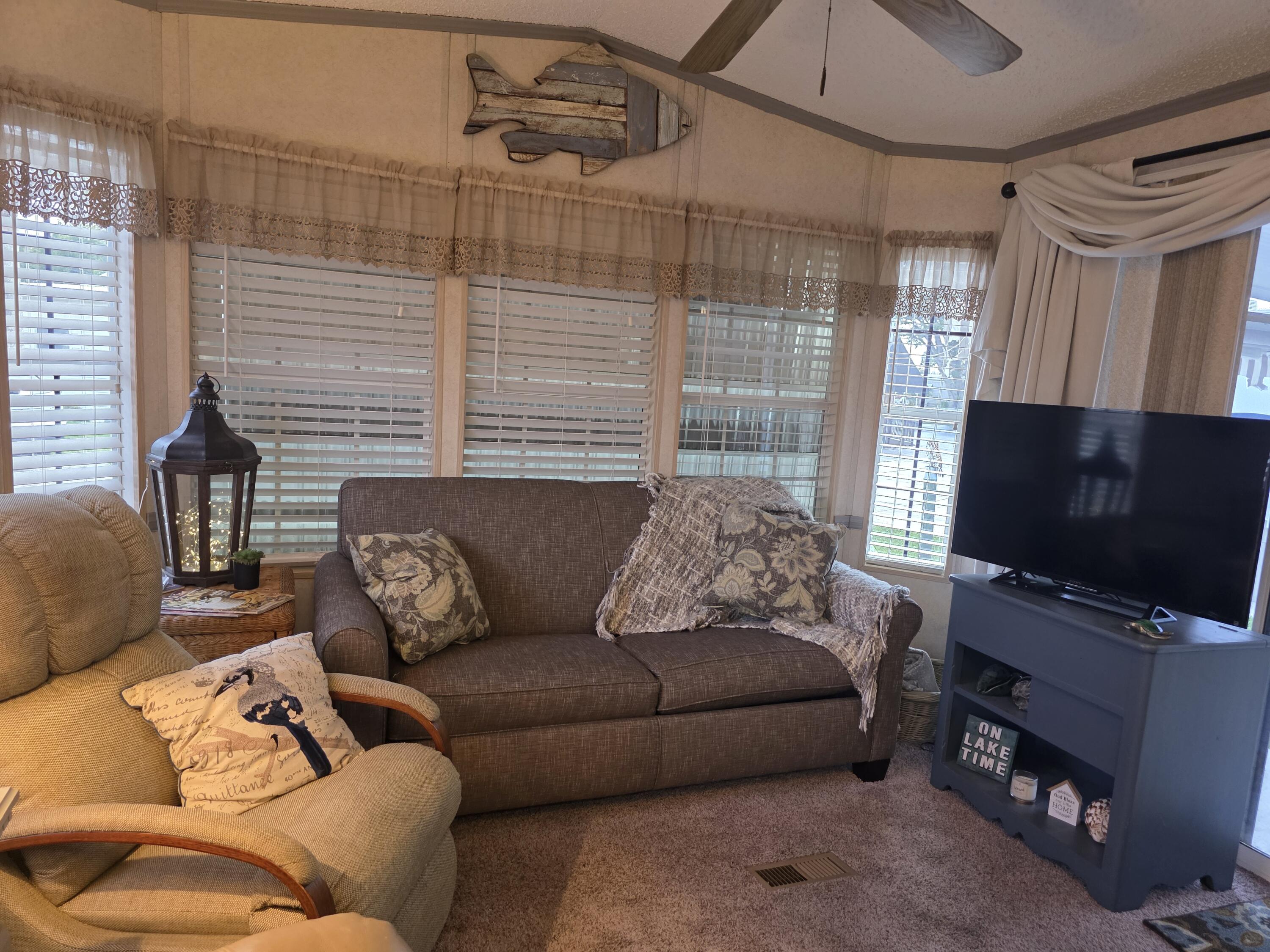 Carpeted living space featuring multiple windows with blinds and valances, a built-in ceiling fan, and a light-toned wall finish