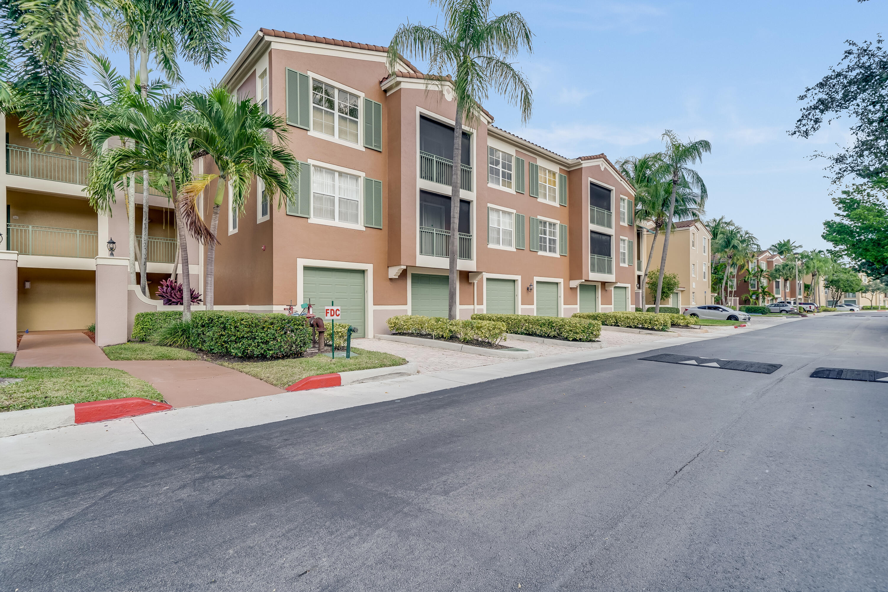 Multi-story Mediterranean-style building with terracotta roof tiles, individual garages, and private balconies featuring screen enclosures