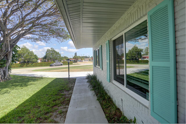 White brick exterior with teal louvered shutters, an extended roofline, and a concrete walkway.