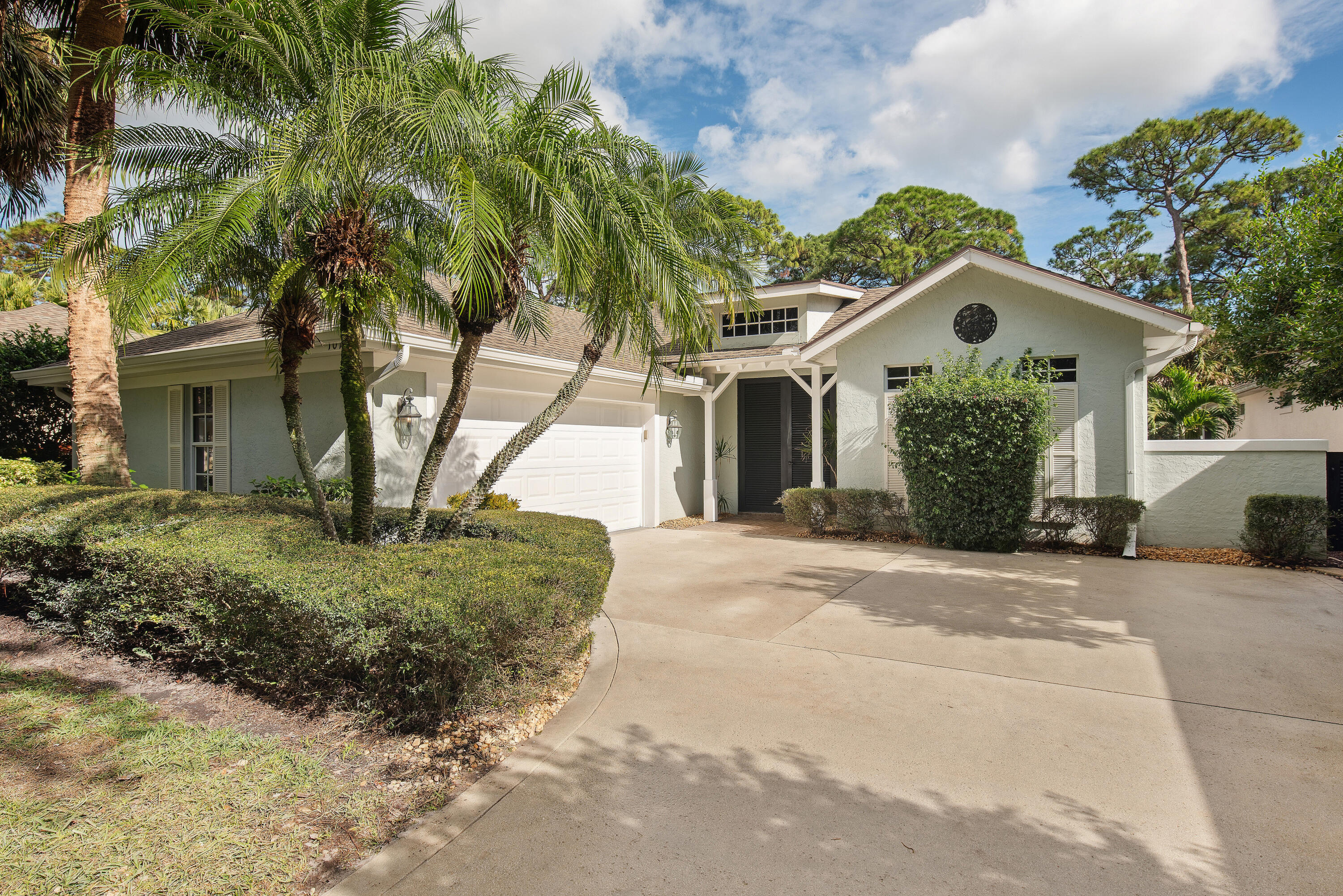 Contemporary single-story residence featuring a clean stucco exterior, arched entryway with circular window detail, and a wide concrete driveway