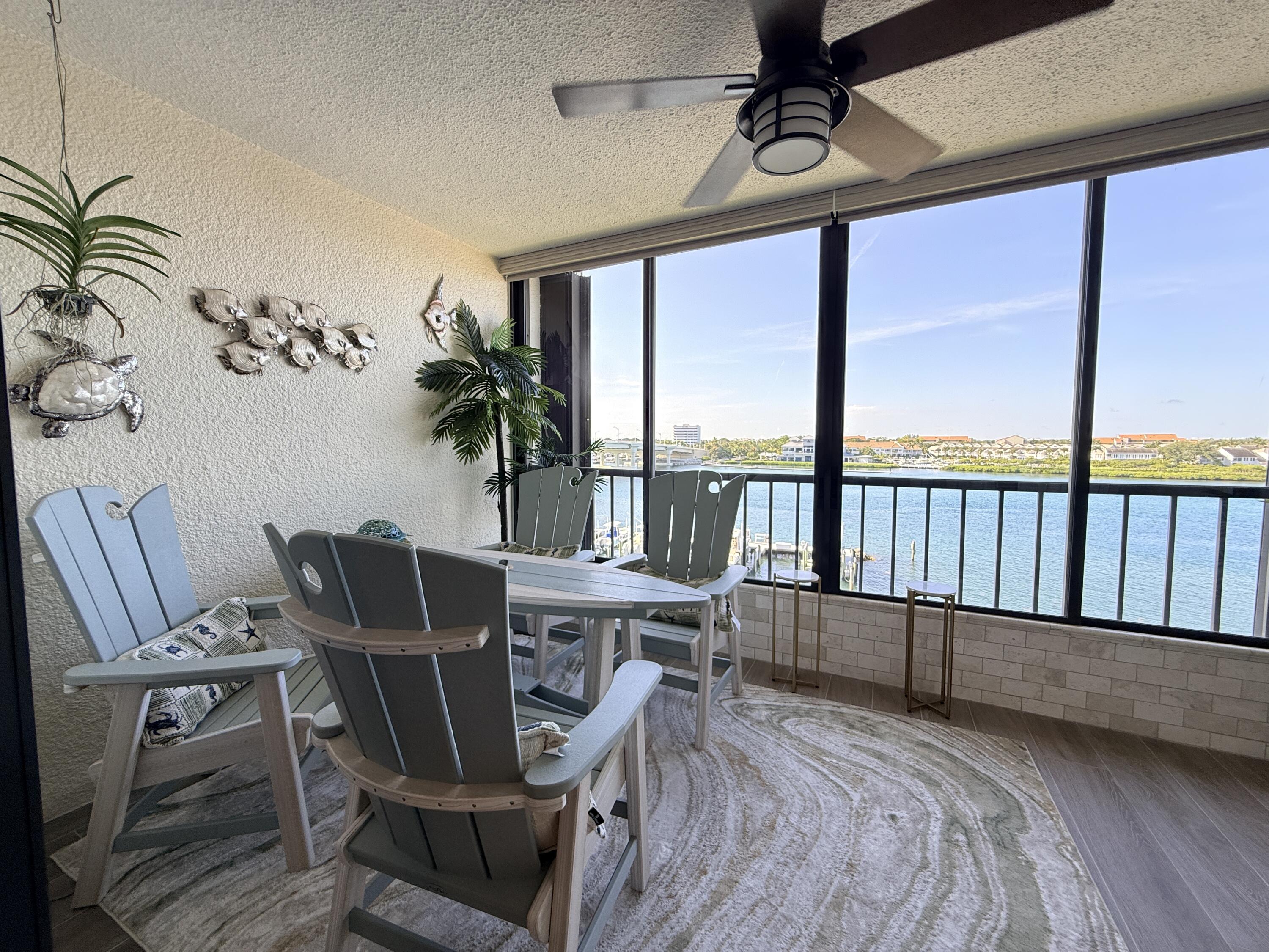 Enclosed balcony featuring expansive water frontage, full-height windows, a ceiling fan, wood-finish flooring, and a tiled half-wall