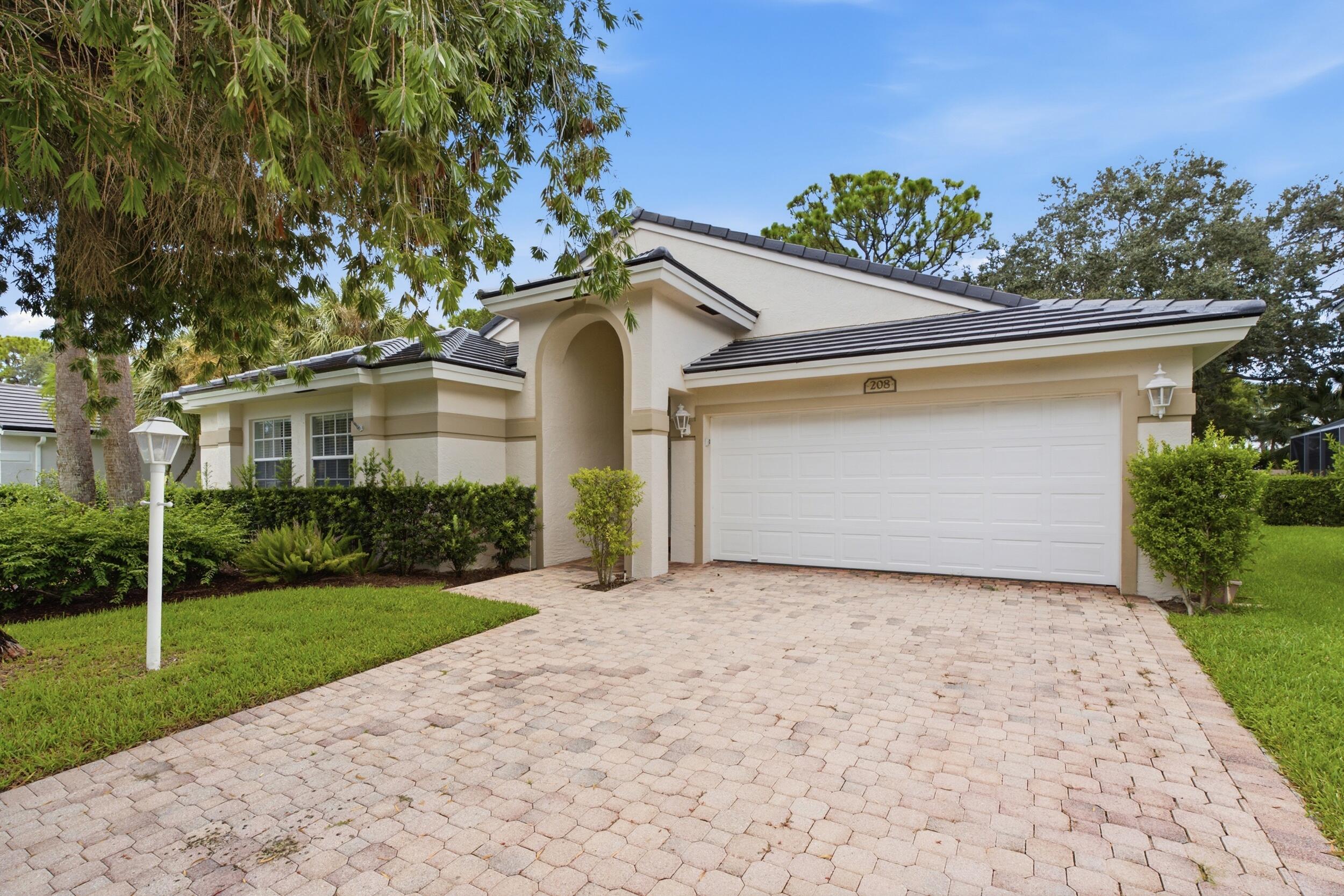 Arched entryway with a dual-car garage, paver driveway, and well-maintained landscaping