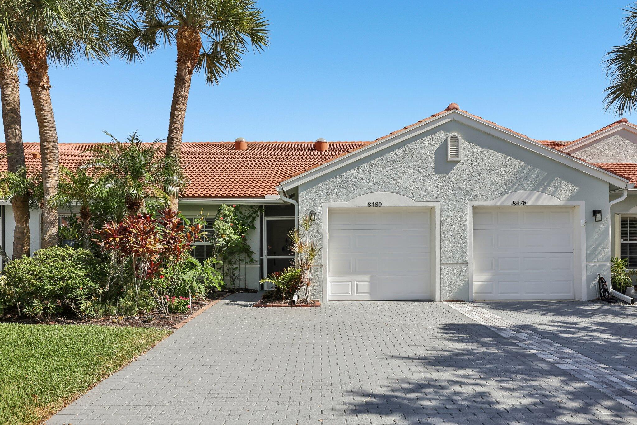 Stucco exterior with a terracotta tile roof, dual garage doors, and a paver driveway