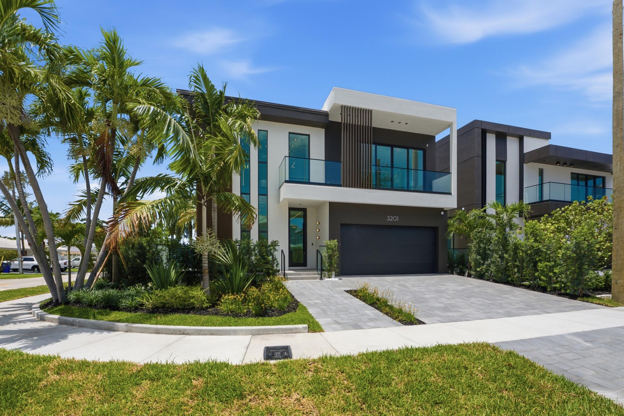 Modern two-story exterior with a flat roofline, glass panel balconies, a paver driveway, and an integrated garage