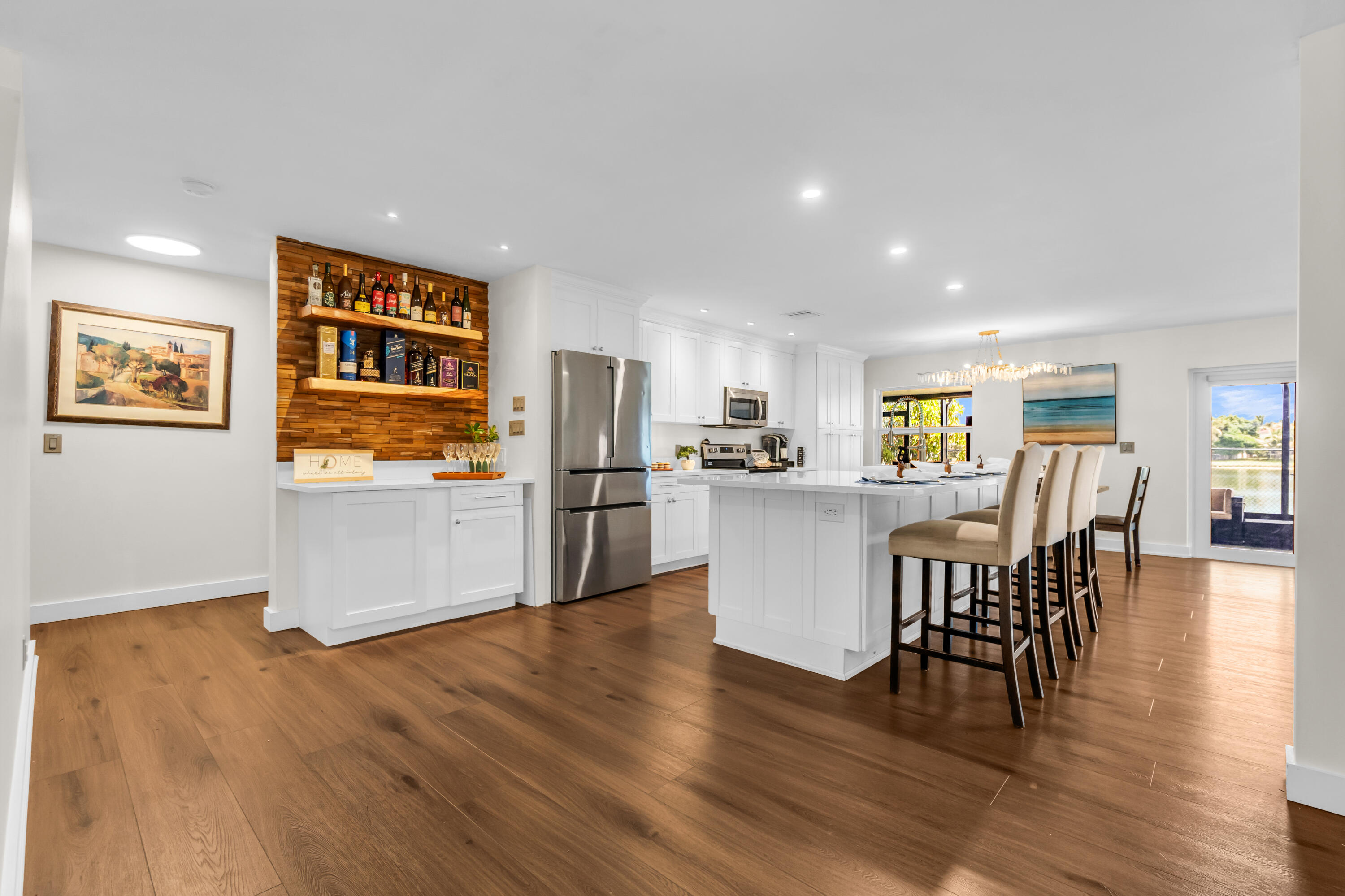 Wide plank wood-finish flooring, white cabinetry, stainless steel appliances, kitchen island with seating, and a built-in beverage bar with wood paneling