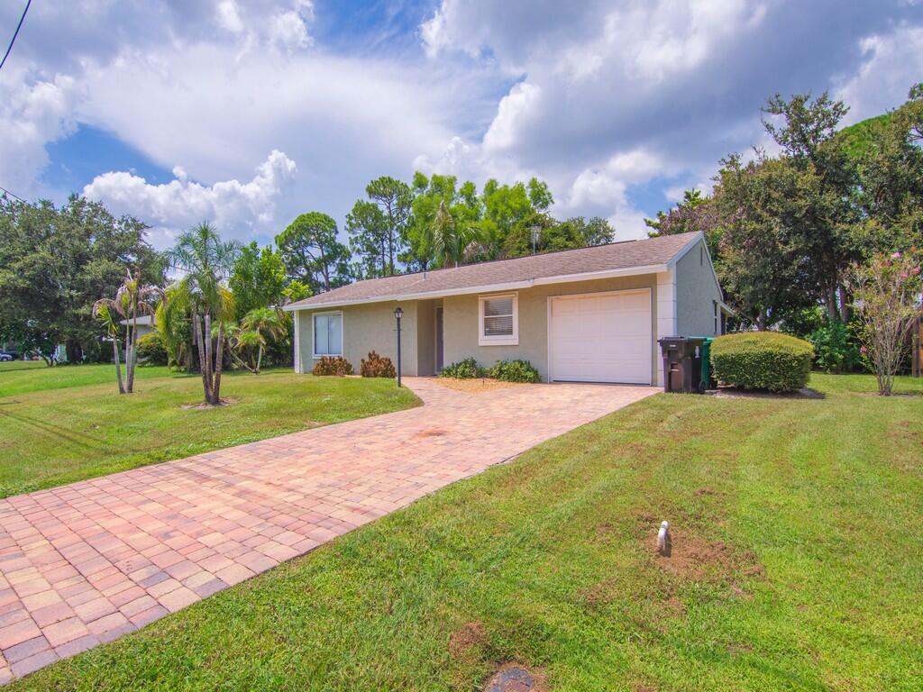 Single-story residence featuring a paver driveway, an attached garage, and mature landscaping