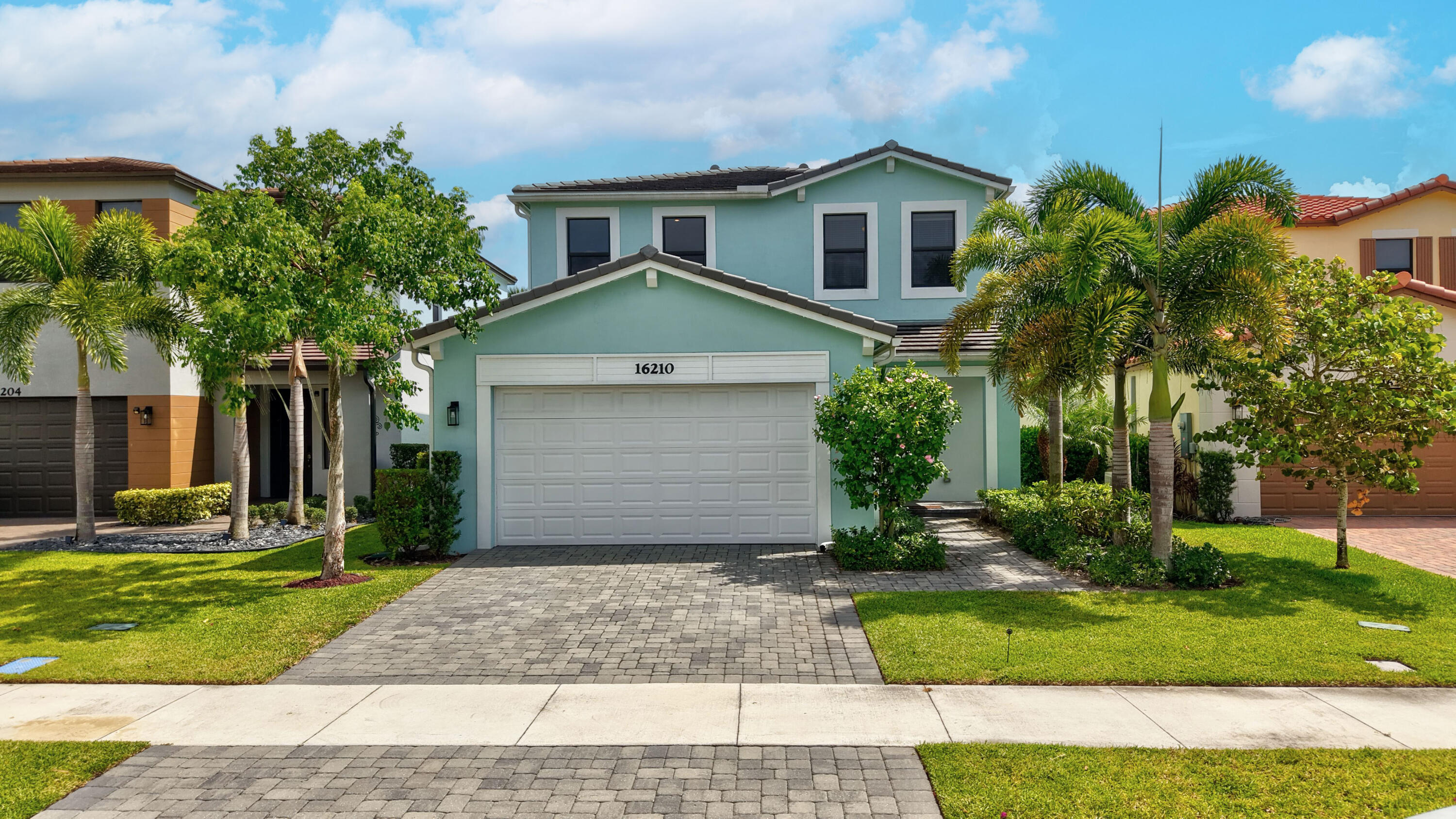 Two-story residence featuring a tile roof, a paver driveway, an integrated garage, and mature landscaping