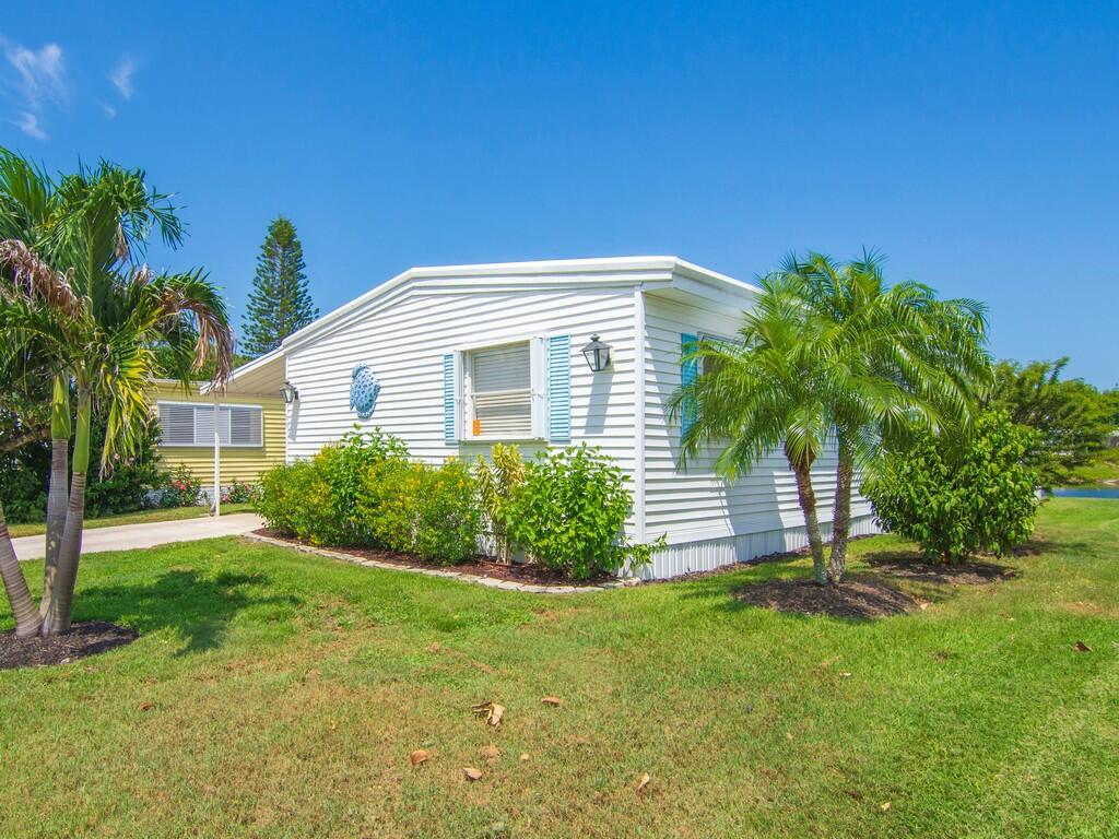 White horizontal siding exterior with blue window shutters, manicured shrubs, and palm trees