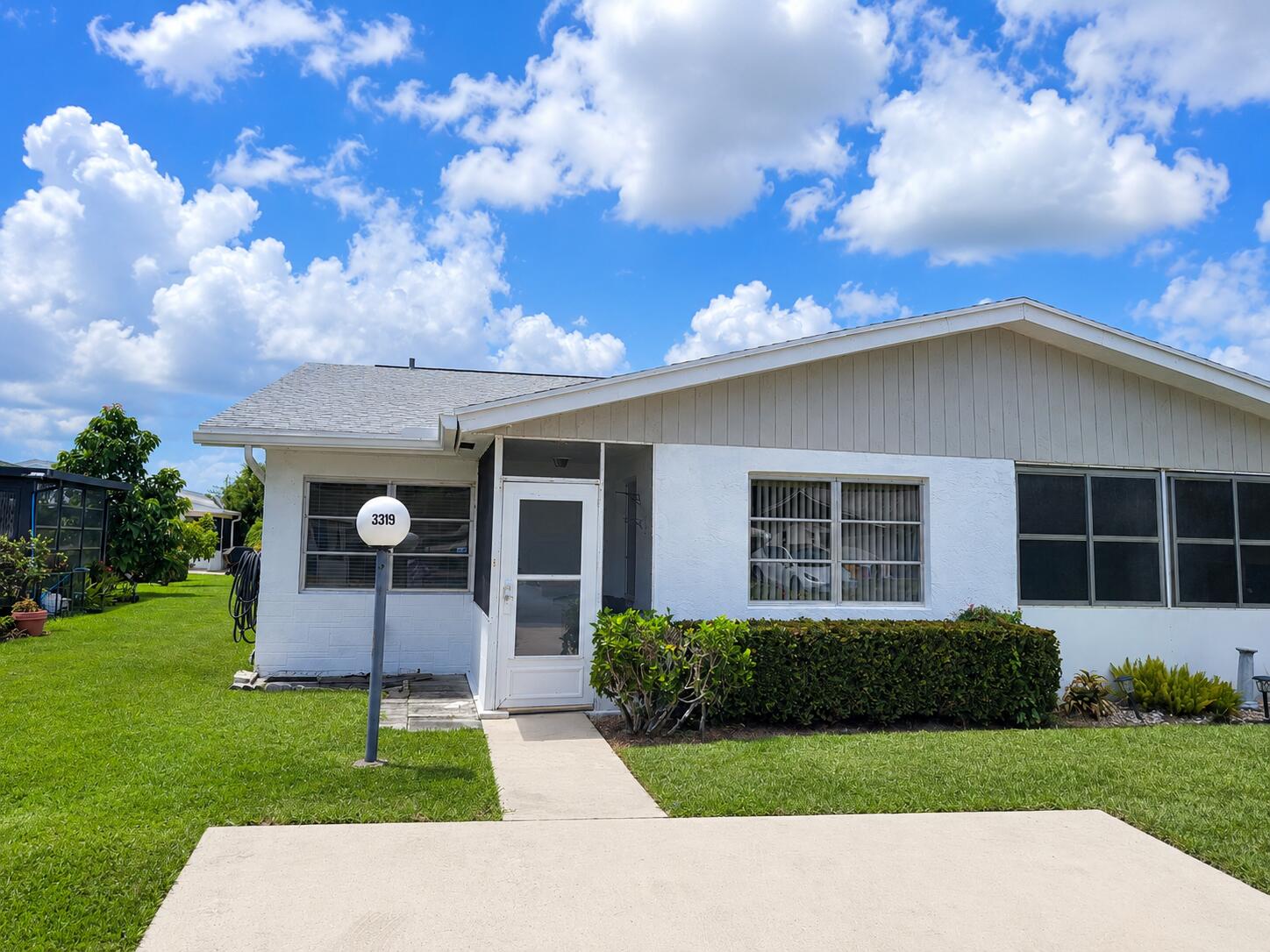 White exterior with stucco and vertical siding accents, featuring a screened entry and a well-maintained lawn