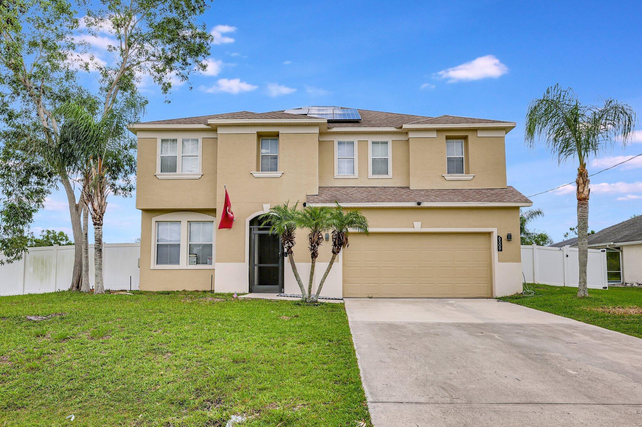 Two-story stucco exterior with an arched entry, attached garage, concrete driveway, and white privacy fencing
