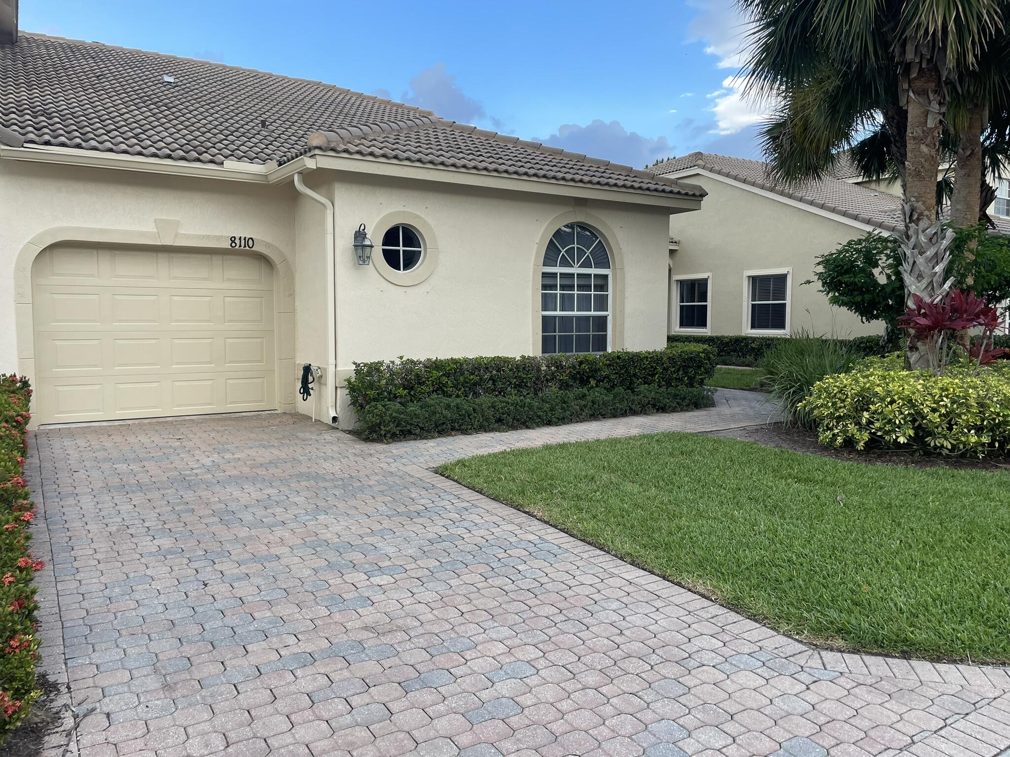 Paver driveway with a curved walkway, stucco exterior, arched window, and tile roof