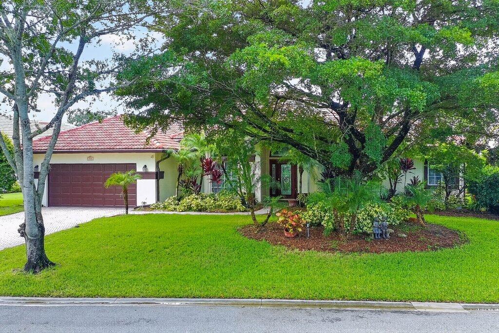 Exterior featuring a tile roof, an integrated two-car garage with a brown door, mature trees, and a landscaped front yard with varied plantings