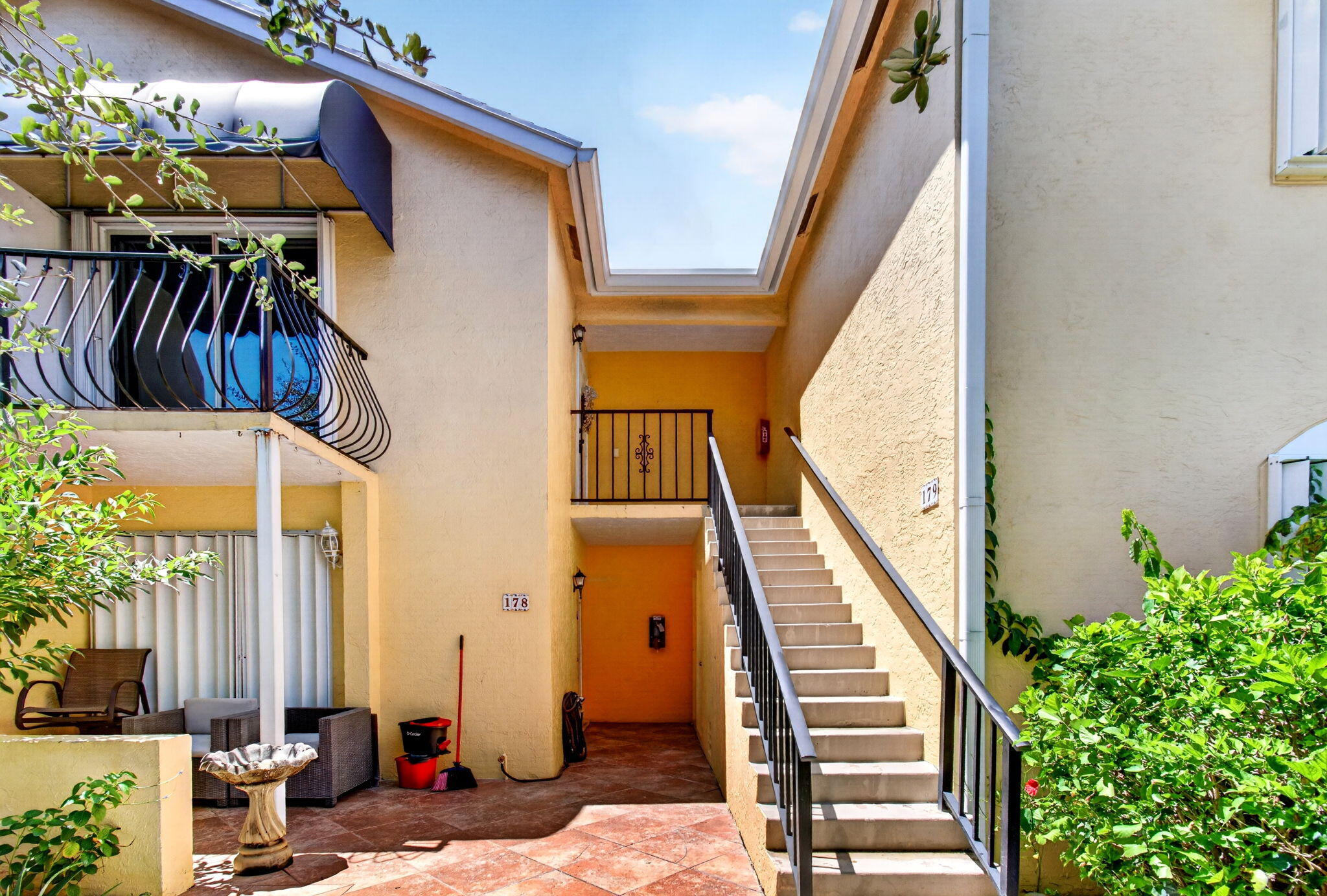 Terracotta-style tile courtyard with stucco exterior and concrete staircase featuring wrought iron railings
