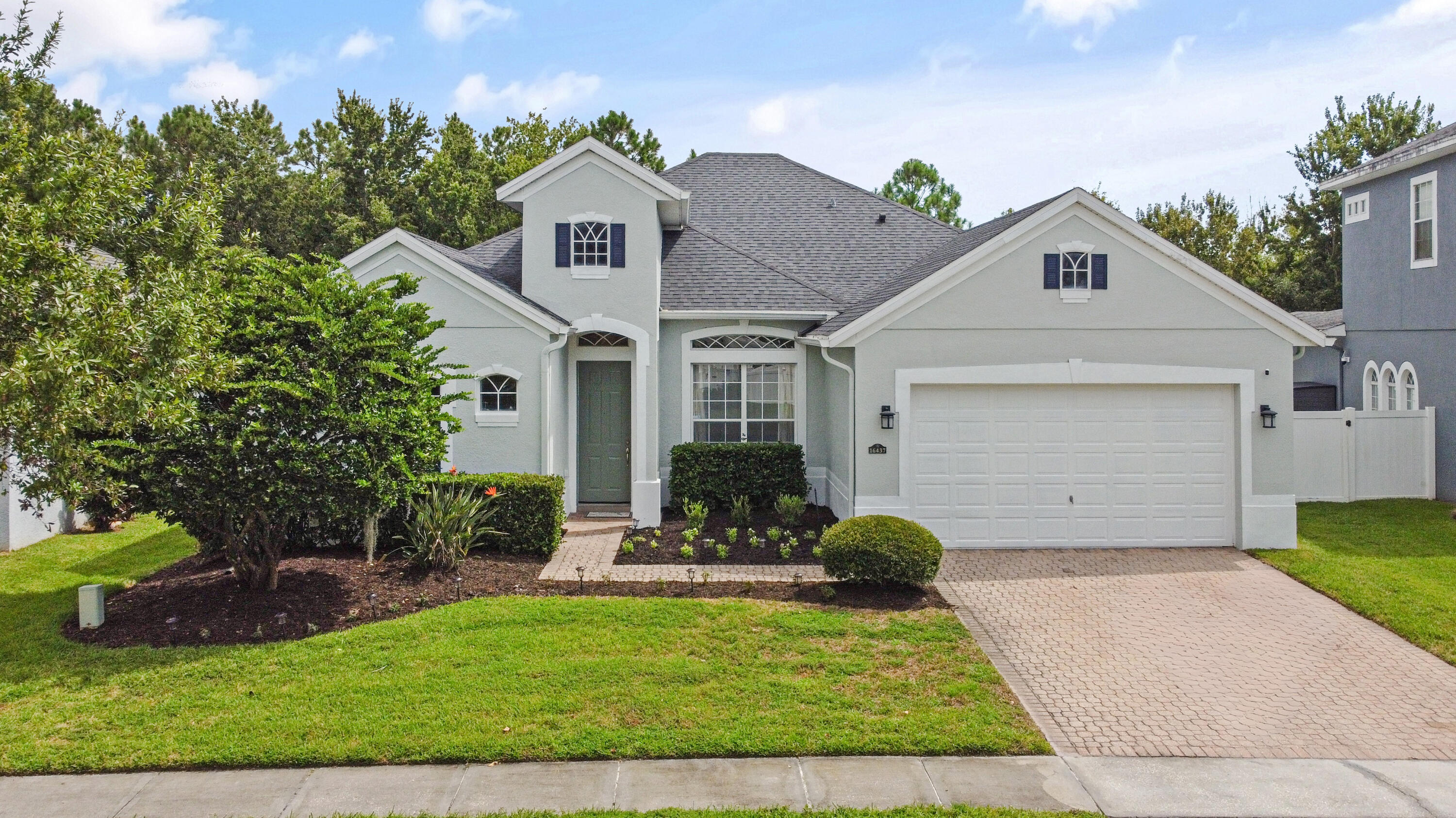 Stucco exterior with a dark shingle roof, arched entryway, a paver driveway, and an attached two-car garage