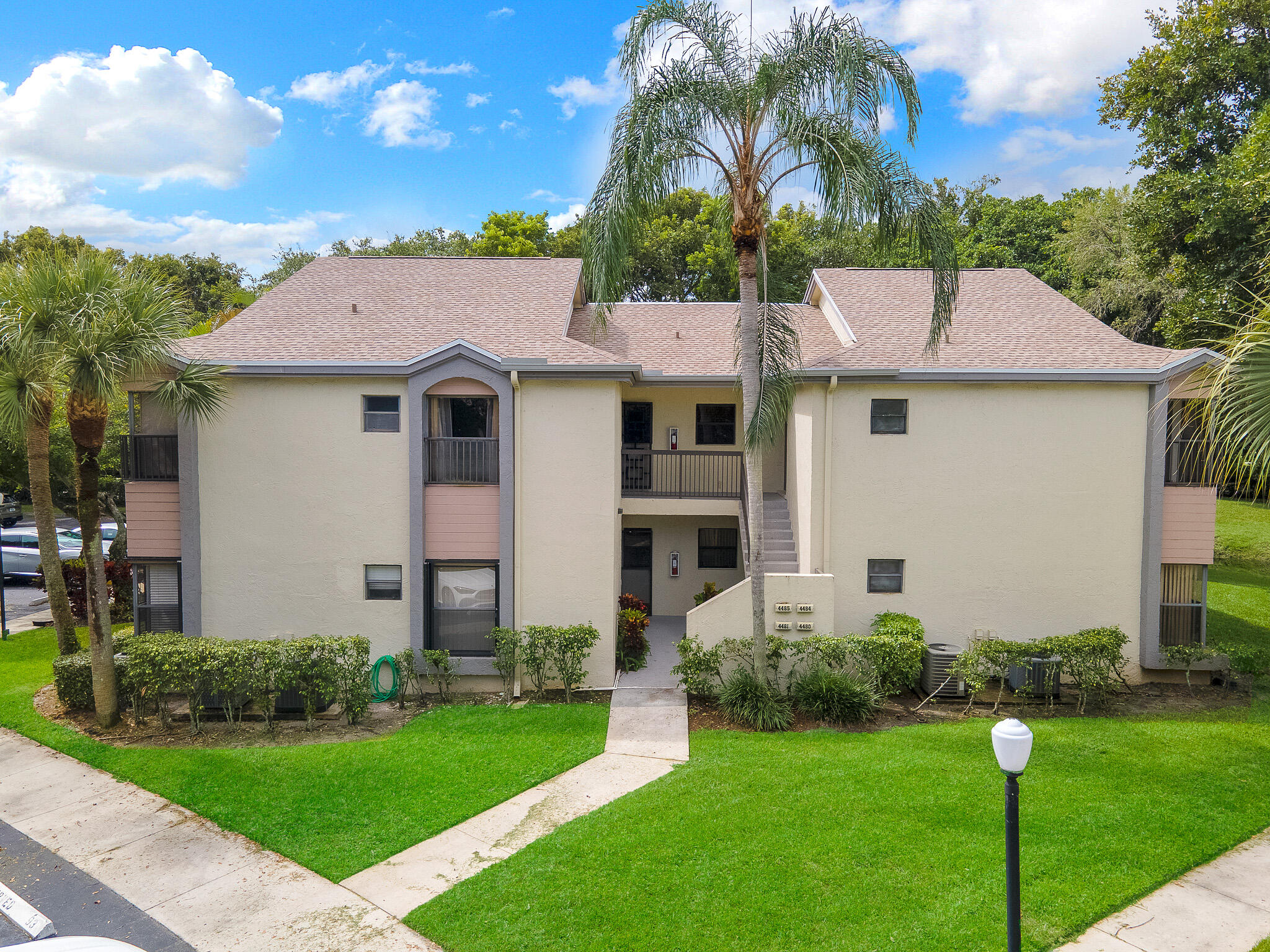 Two-story stucco exterior with a multi-gable roof, mature palm trees, manicured shrubbery, and a concrete walkway