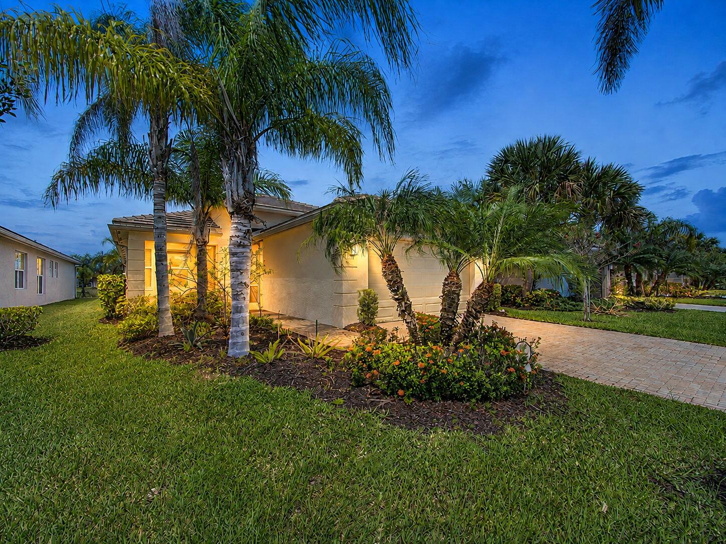 Stucco exterior with a tile roof, mature palm trees, landscaped shrubbery, and a paver driveway