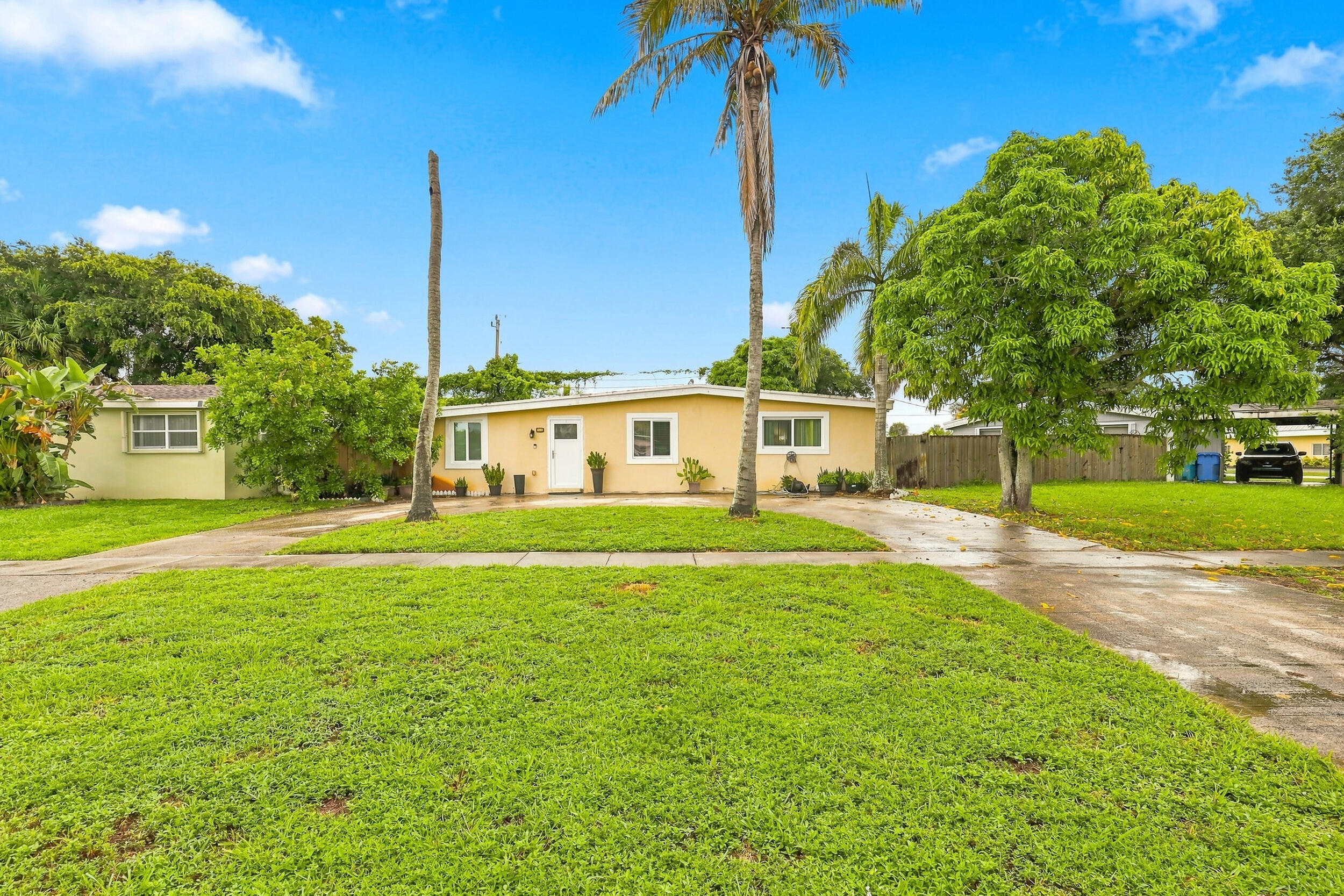 Wide front view showcasing the home, spacious lawn, mature trees, and driveway.