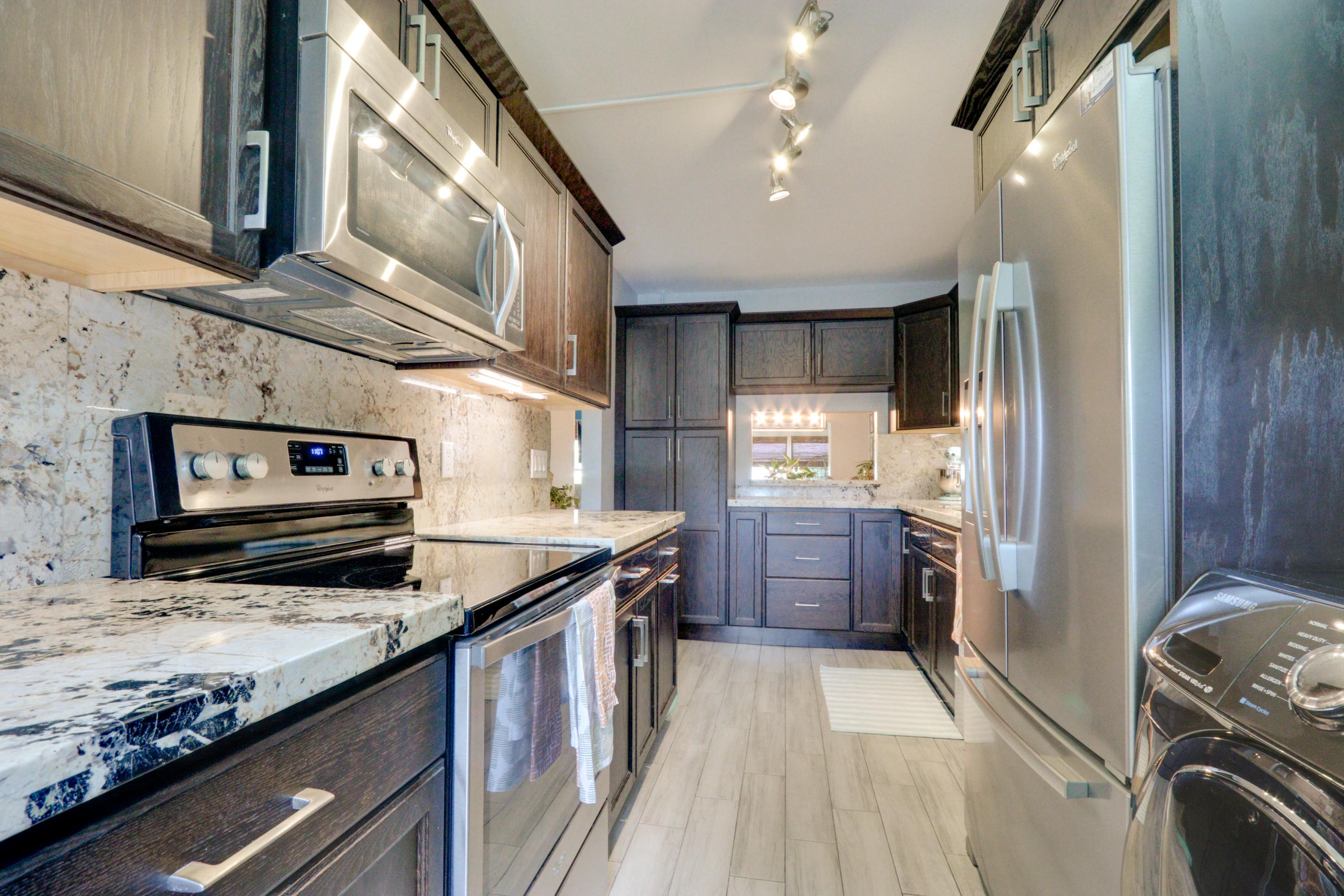 Kitchen featuring dark wood-finish cabinetry, stainless steel appliances, speckled stone countertops, and wood-finish flooring