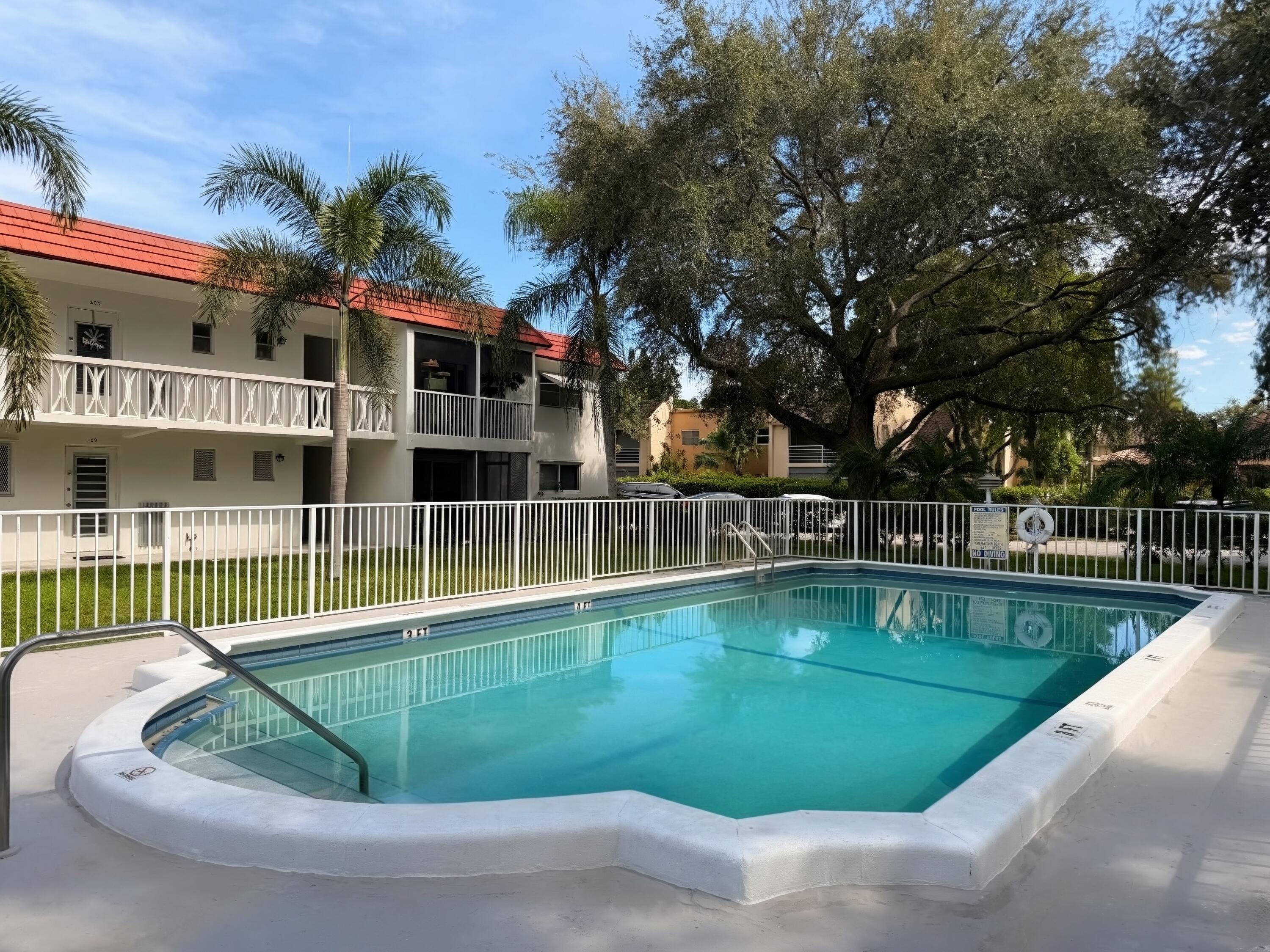 Outdoor swimming pool with integrated steps, surrounding paved deck, and adjacent white metal fencing