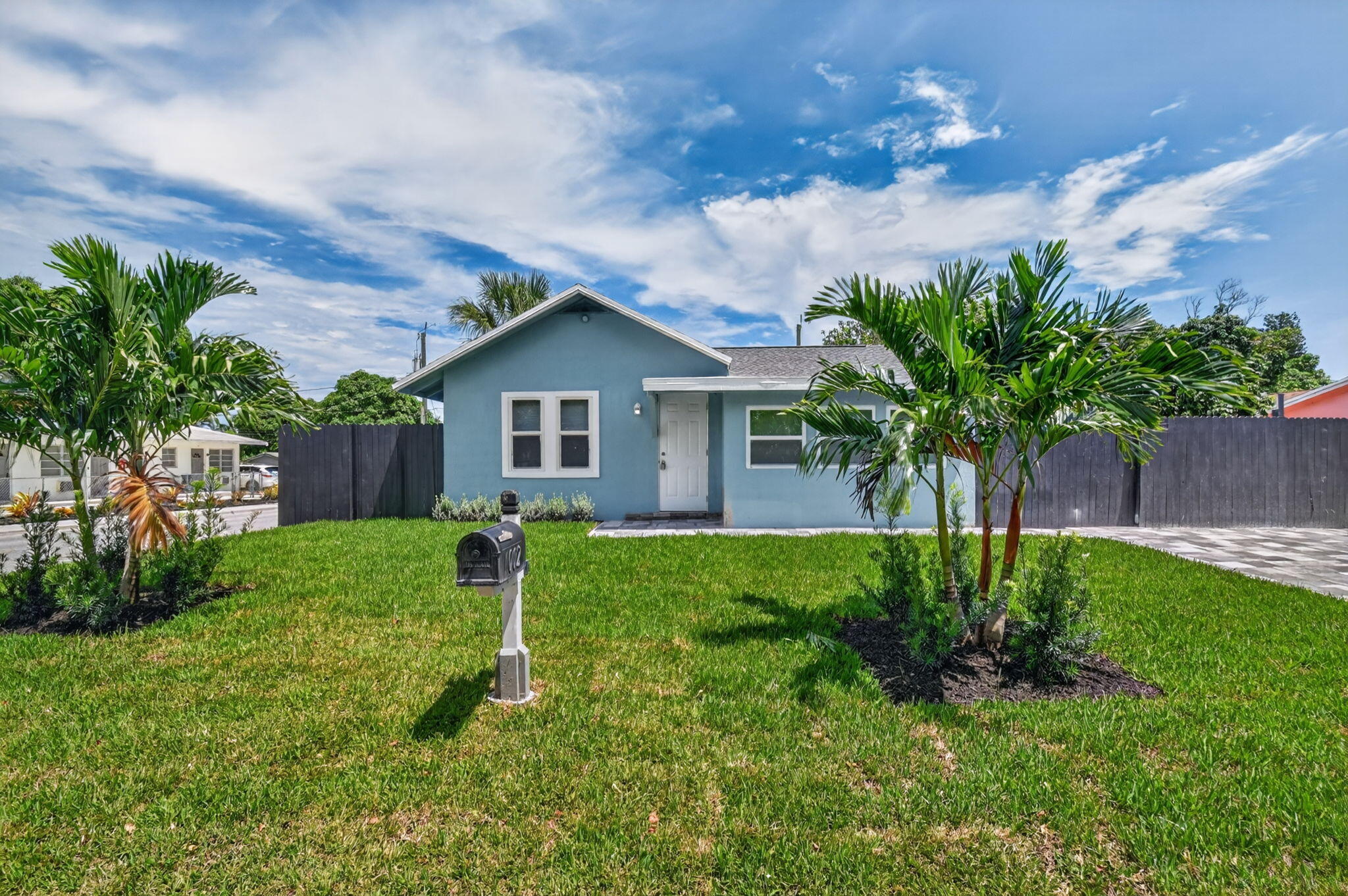 Light blue exterior with white trim, well-maintained lawn, mature palm trees, and a dark privacy fence