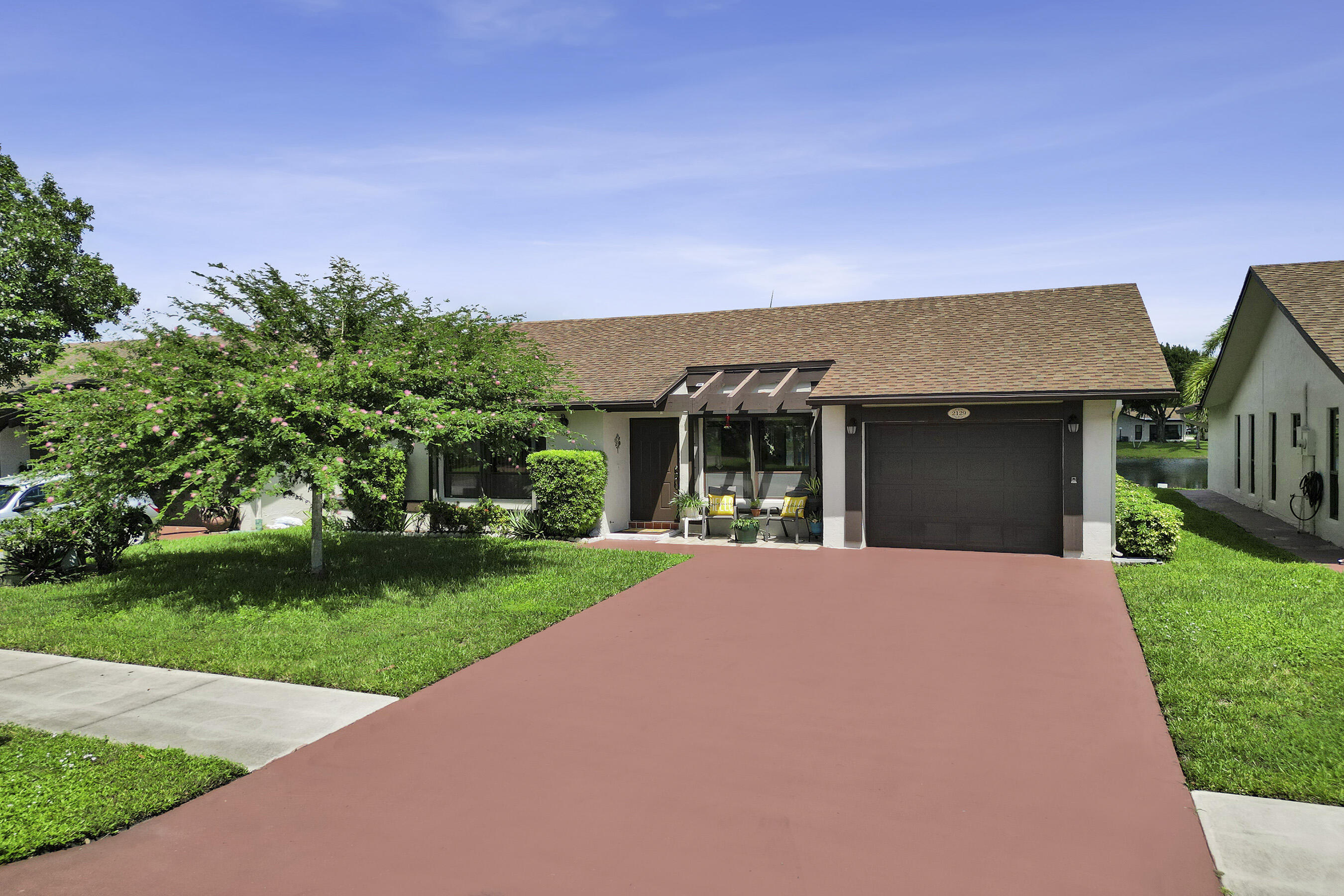 Single-story residence featuring a brown asphalt shingle roof, a brown garage door, and a pergola accen