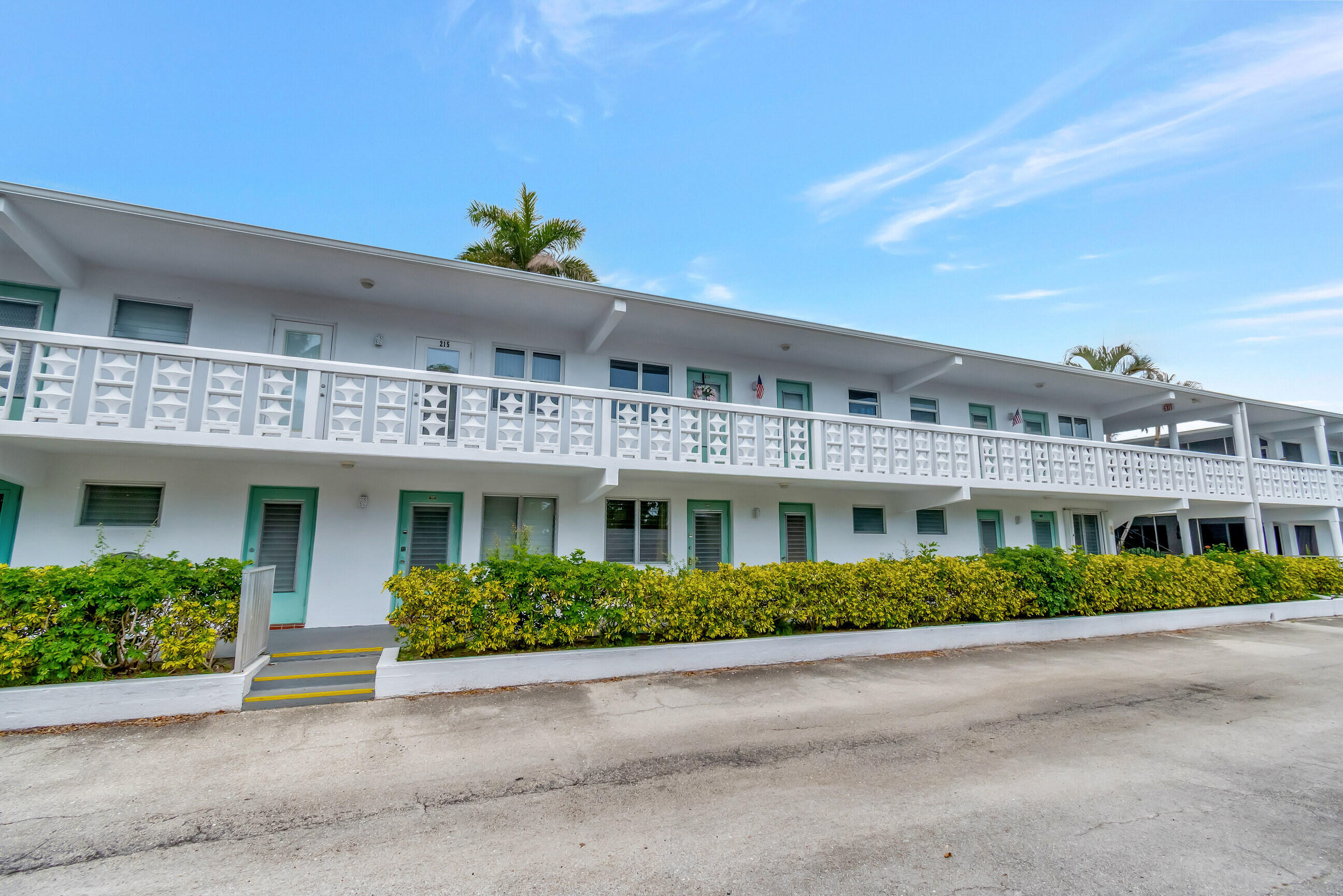 Multi-story building featuring white exterior, patterned balcony railings, and teal-framed entryways