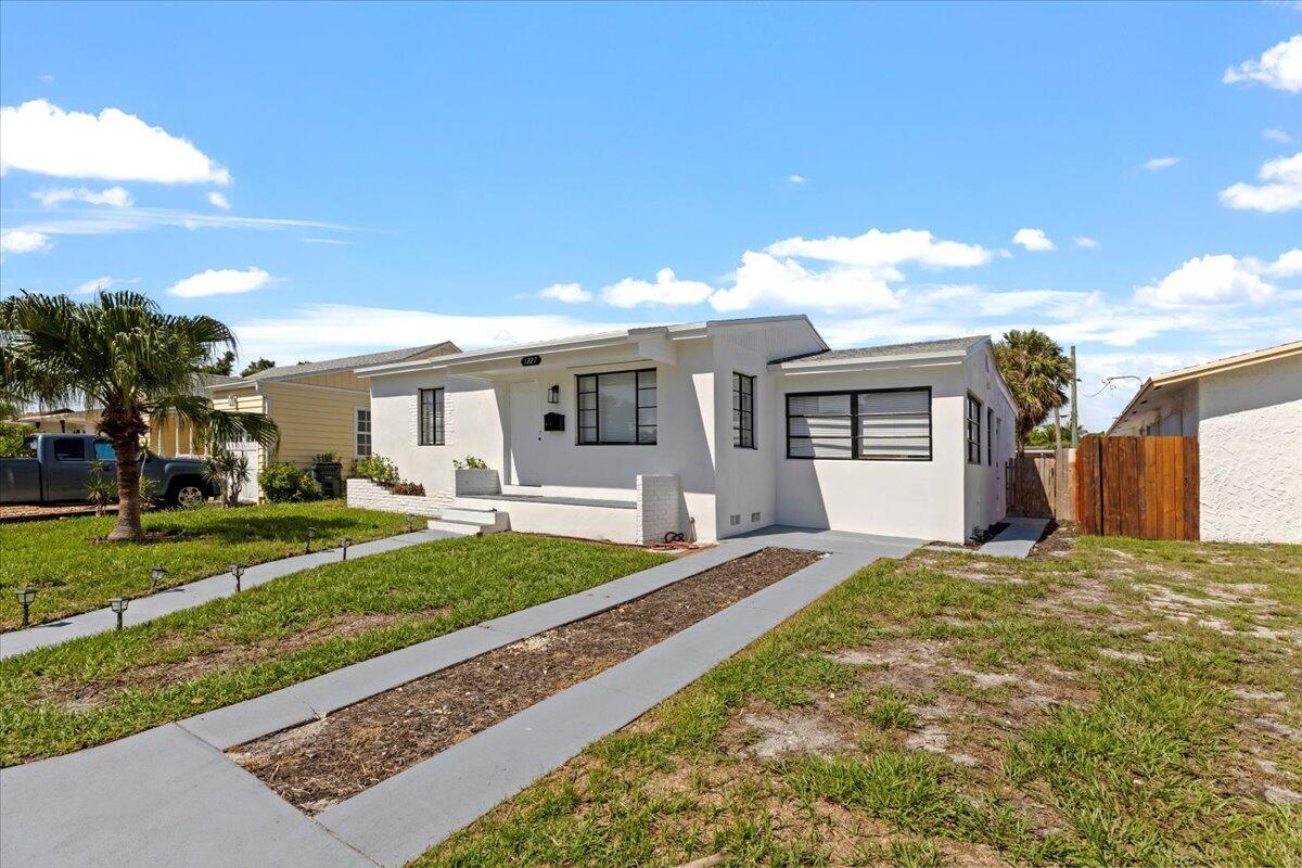 White stucco exterior with dark-framed windows, a palm tree, a wooden fence, and a concrete driveway
