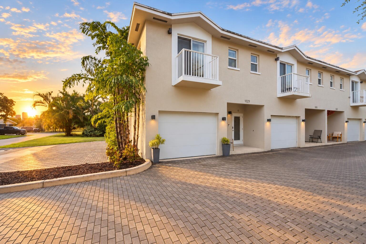 Modern townhome exterior with balconies, individual garage doors, paver driveway, and lush landscaping