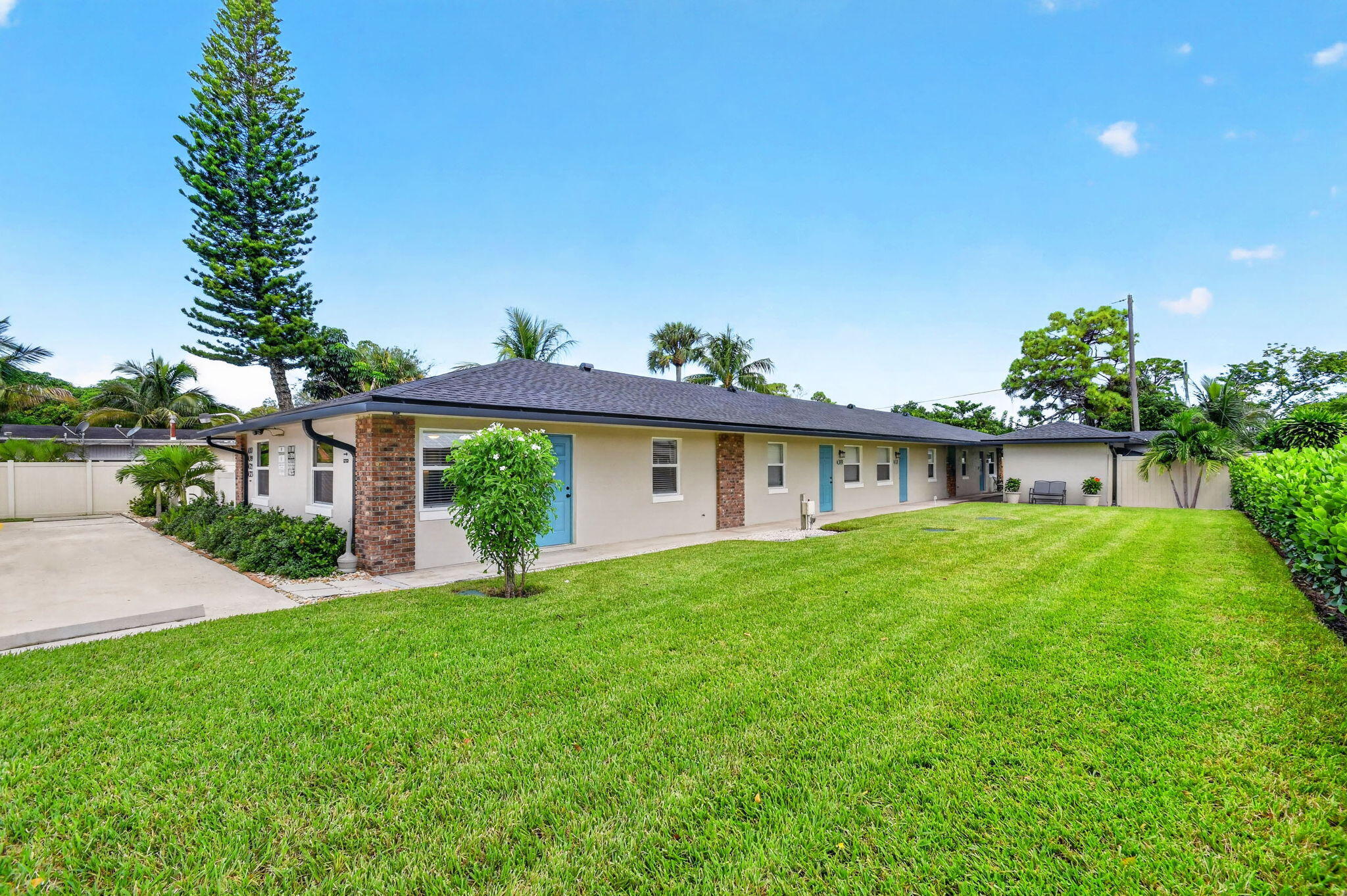 Expansive lawn with mature landscaping, a long paved driveway, brick accents, and vibrant blue entry doors