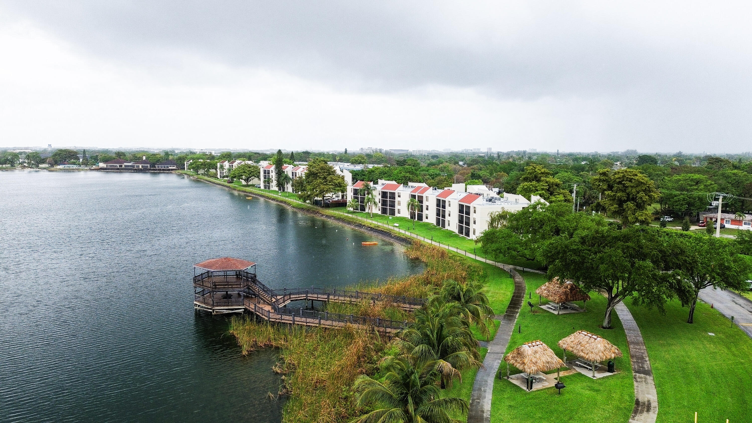 Waterfront property featuring a private dock with a covered gazebo, multiple shaded picnic areas, mature landscaping, and a paved walking path
