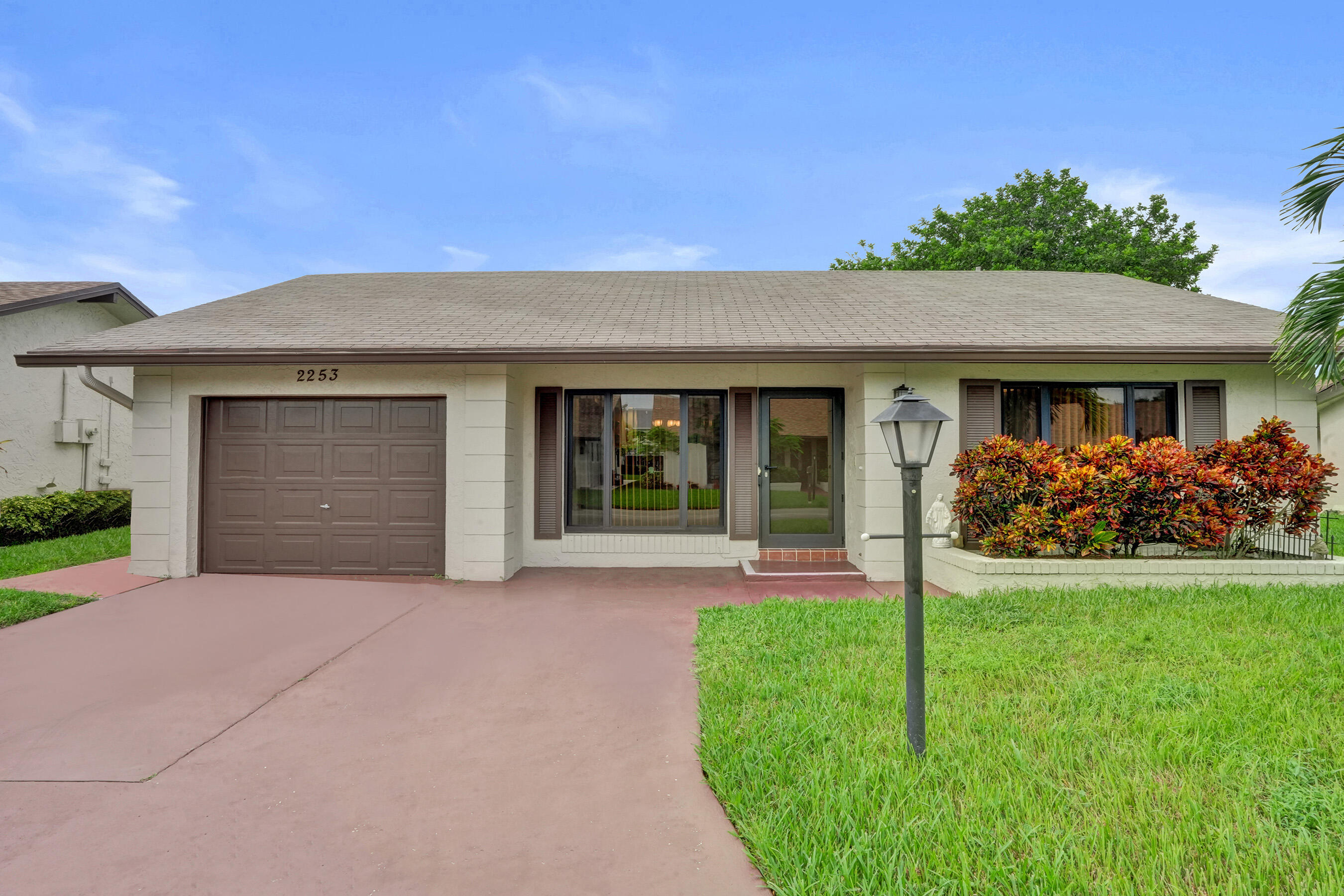 Single-story residence featuring a brown garage door, front entry, landscaped shrubbery, and a paved driveway
