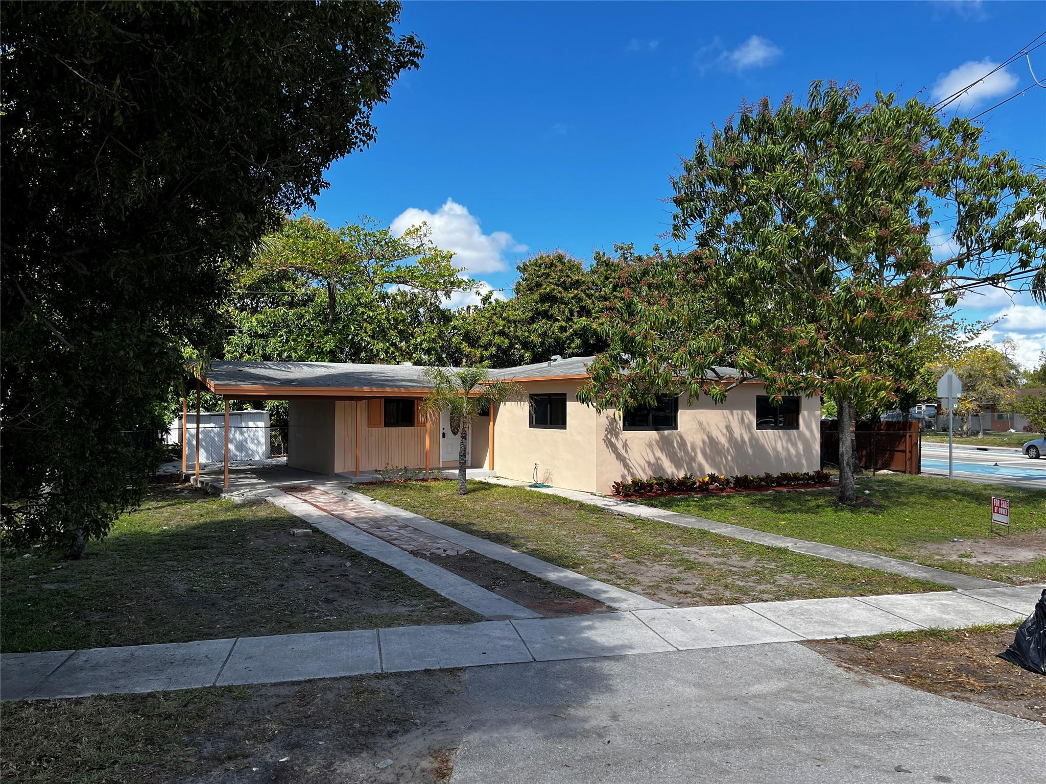 Single-story residence featuring stucco exterior, covered carport, and mature trees