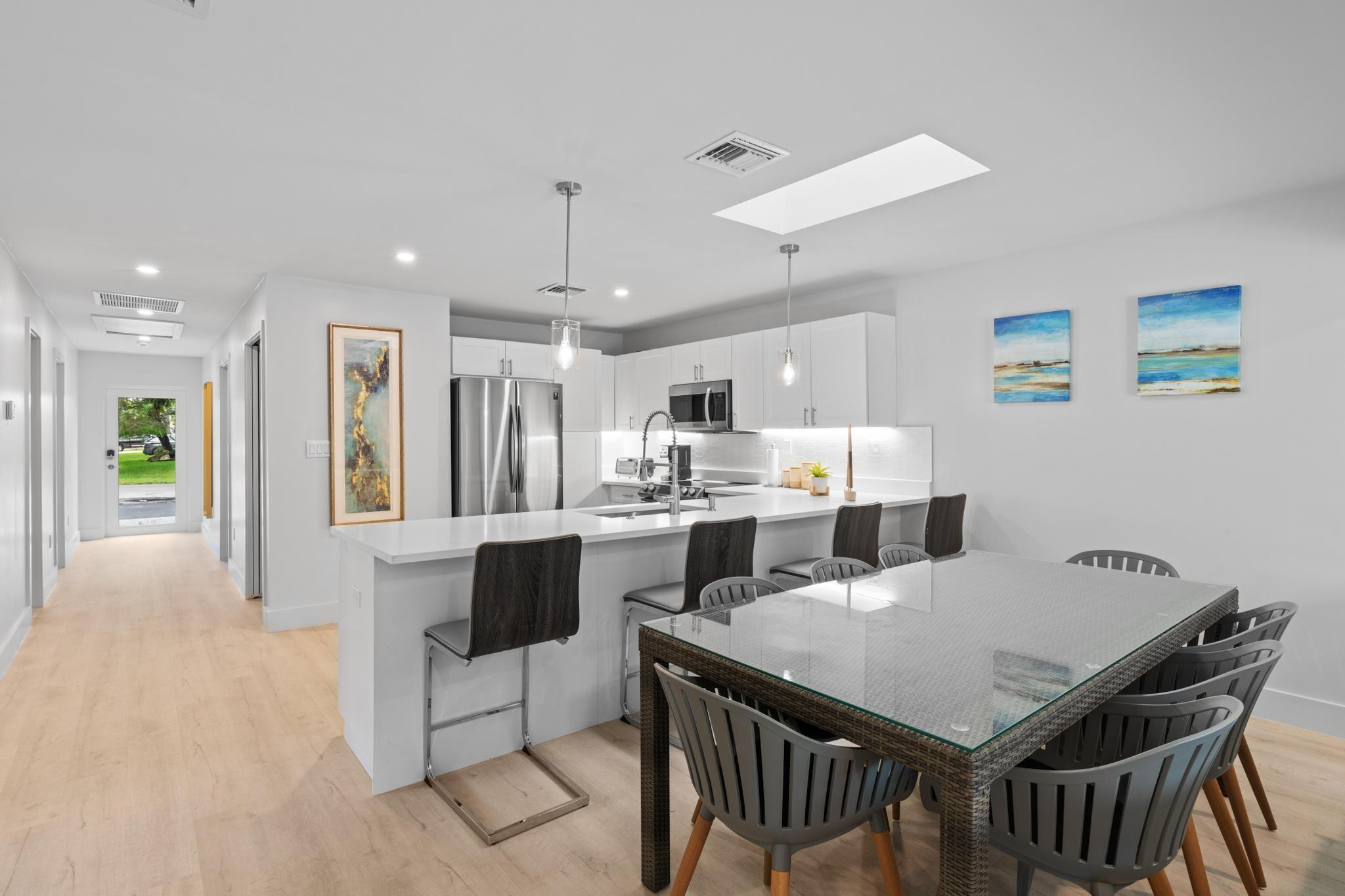 Open-concept kitchen and dining area featuring light wood-finish flooring, white cabinetry, stainless steel appliances, and a central island with countertop seating