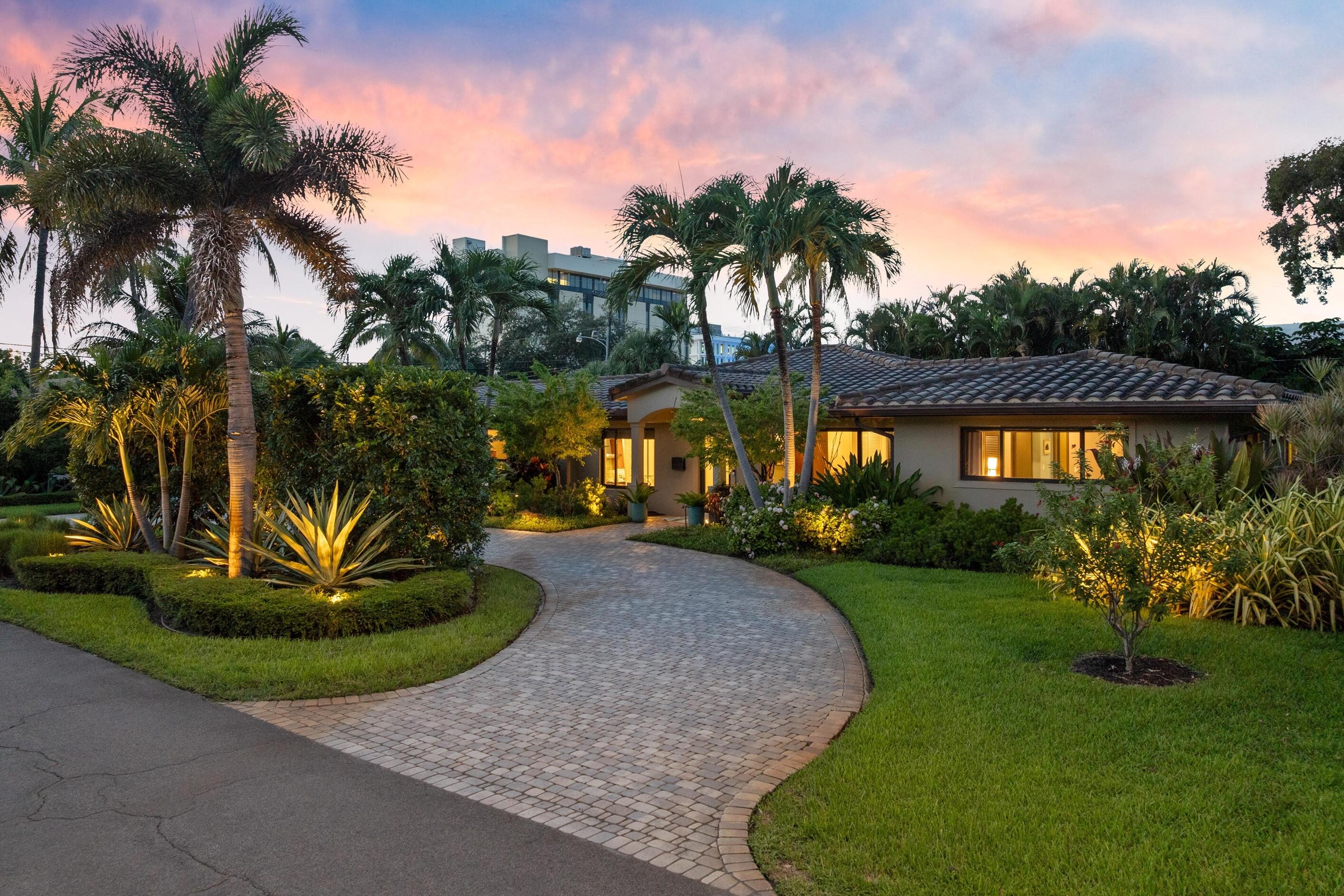 Paver driveway, lush landscaping, mature palm trees, exterior lighting, and a tile roof