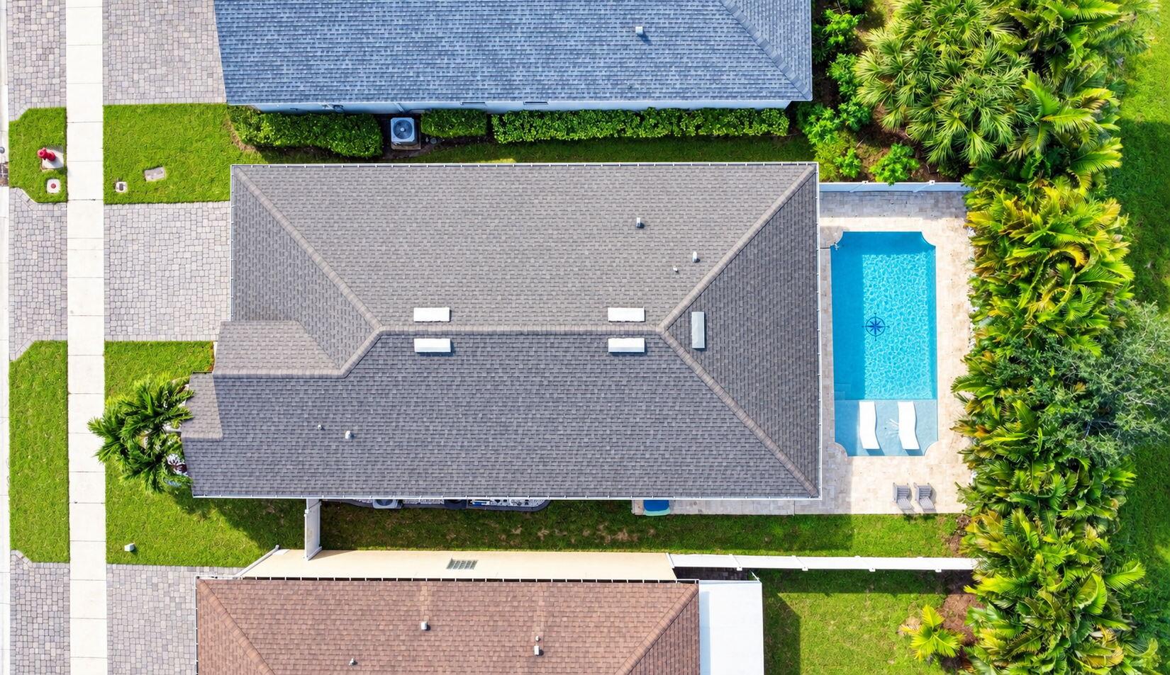 Rectangular swimming pool with a paved deck, surrounded by lush landscaping and a shingle roof