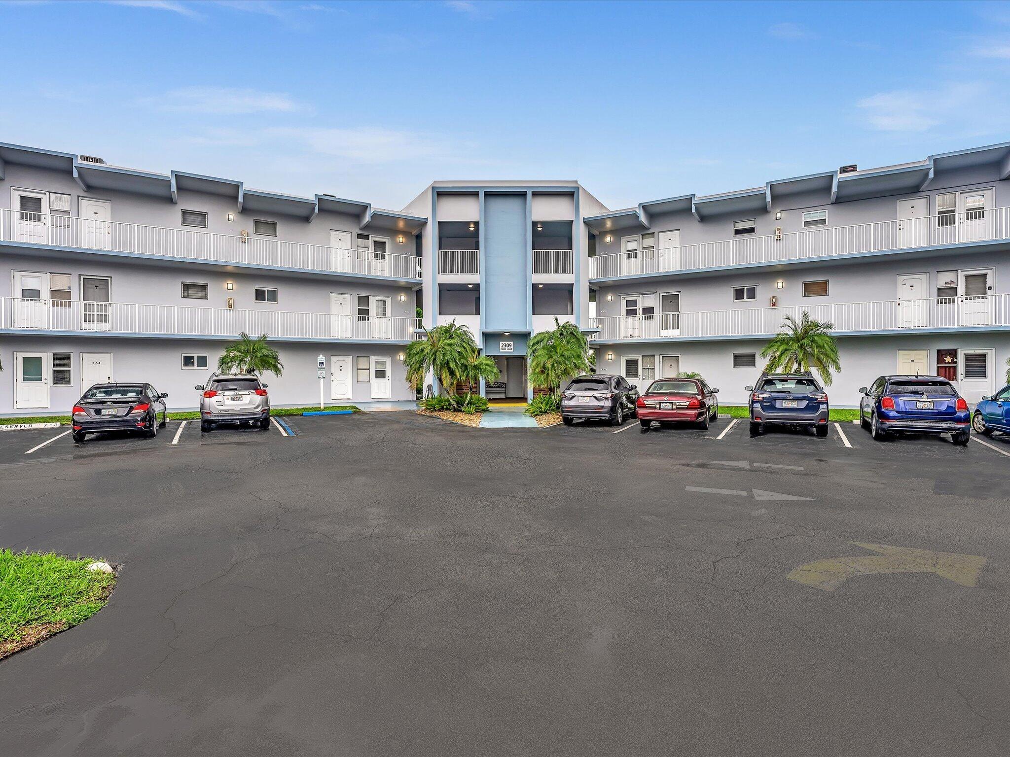 Multi-story building with exterior corridors, a central entrance, and a paved parking area