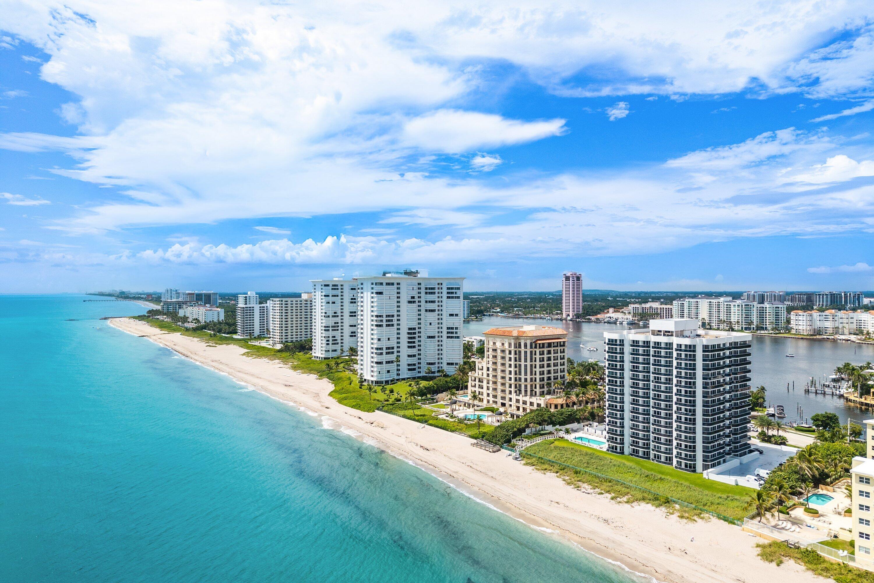 Expansive coastline featuring a sandy beach, multiple high-rise buildings, and a wide waterway with docked boats