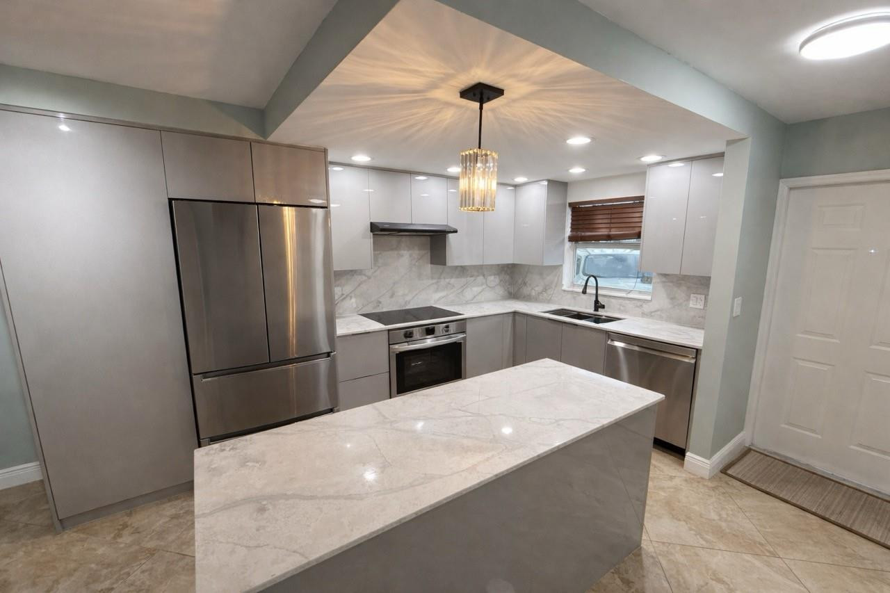 Kitchen featuring an island with a light-toned countertop, stainless steel appliances, light gray cabinetry, and a crystal pendant light