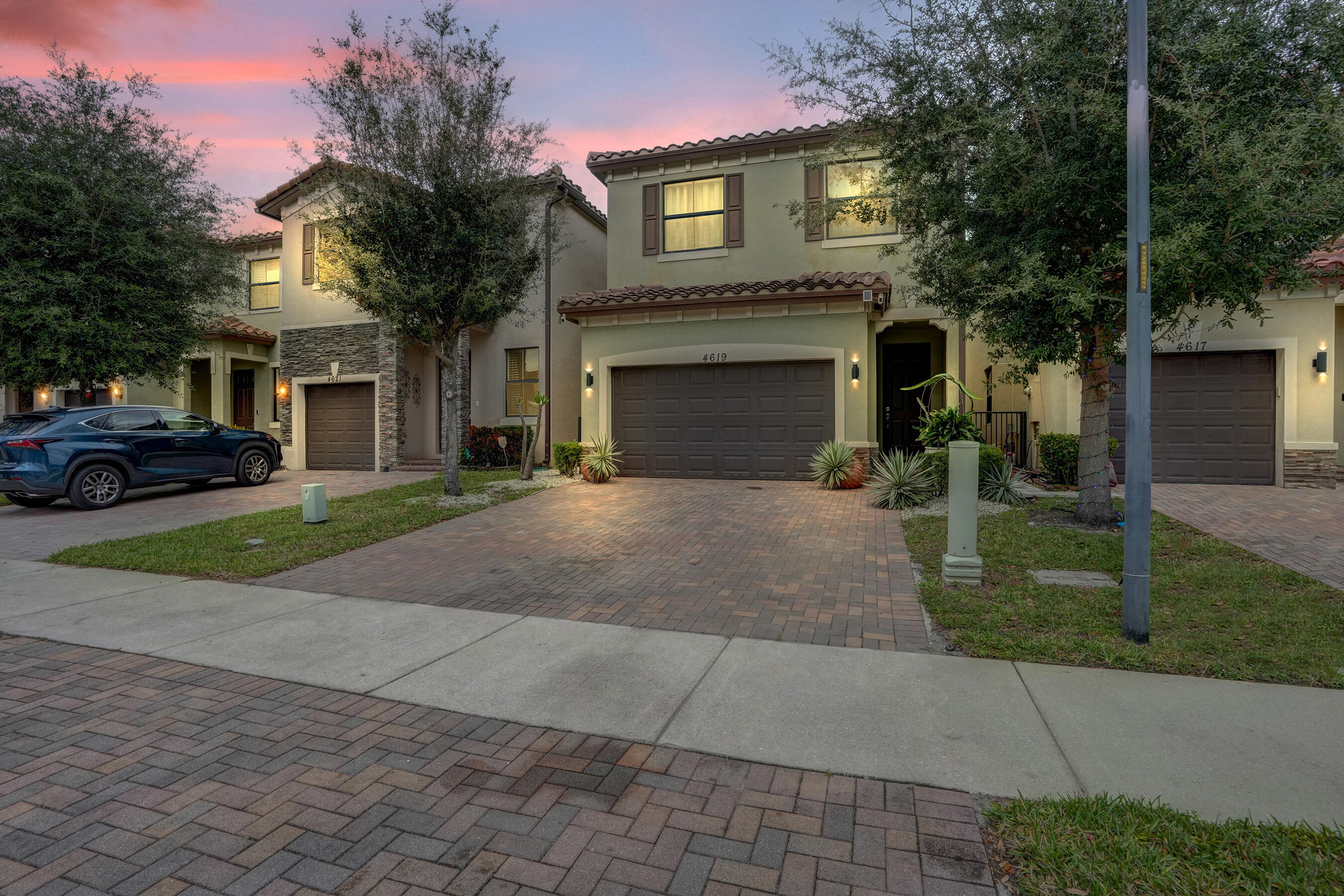 Stucco exterior with stone accents, tile roof, attached garage, and paver driveway