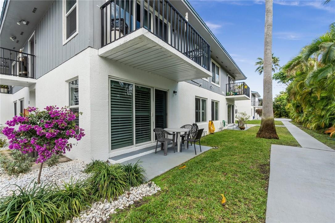 Ground-floor patio with sliding glass doors, surrounded by lush landscaping and a concrete pathway