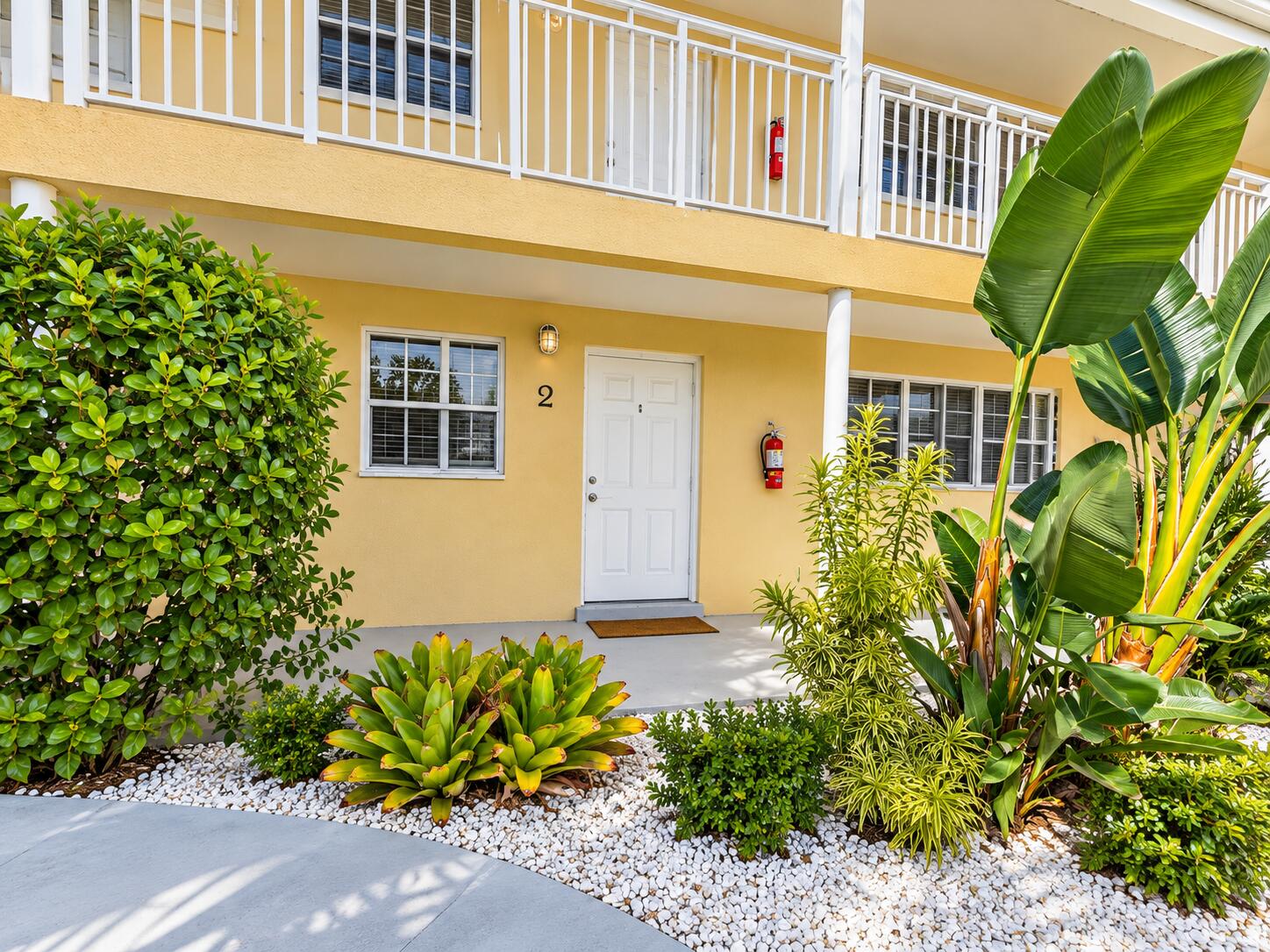 Tropical landscaping with white gravel accents, featuring a light yellow exterior and white architectural railings