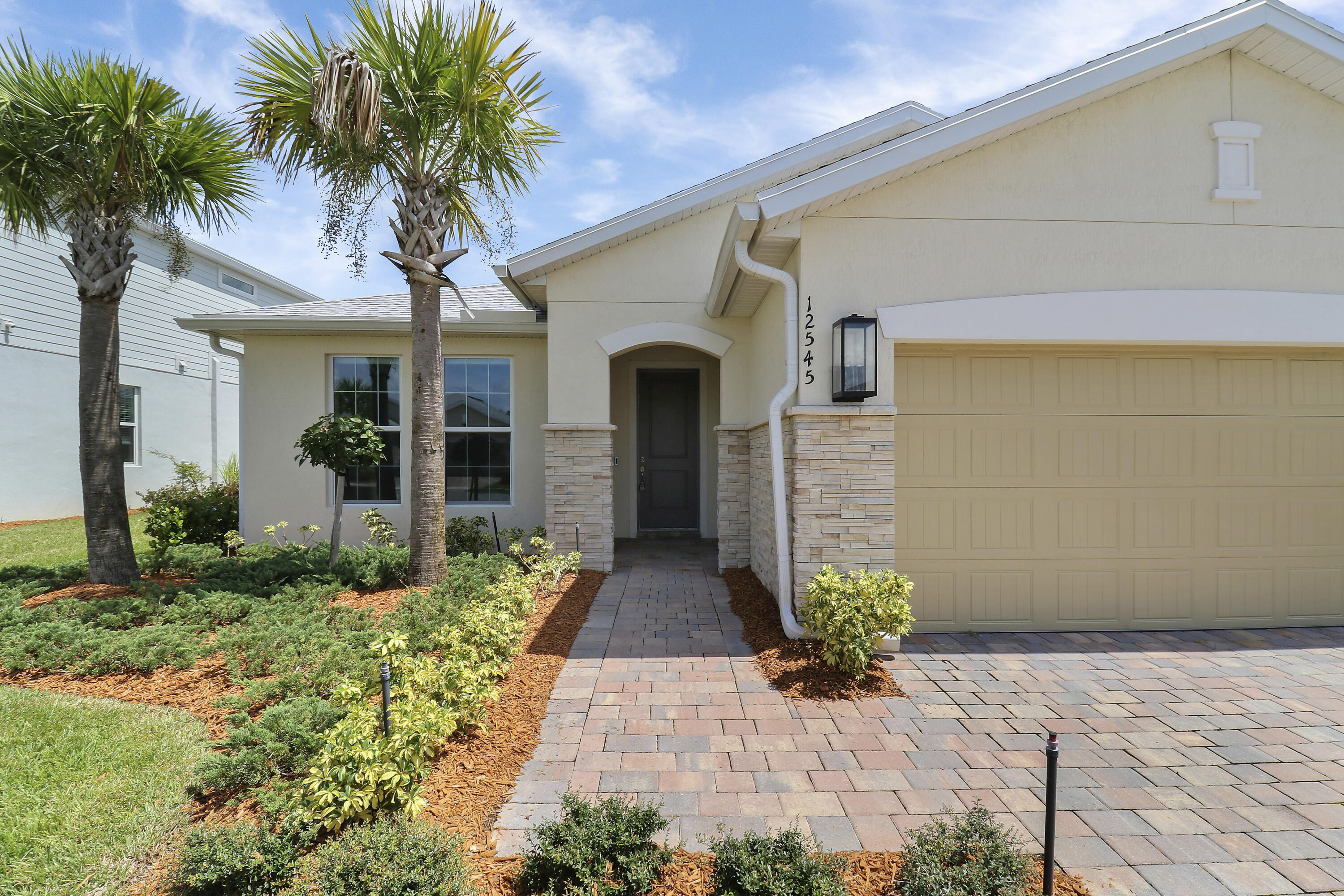Stucco exterior with stone accents, paver driveway, paver walkway, integrated garage, and landscaped front yard