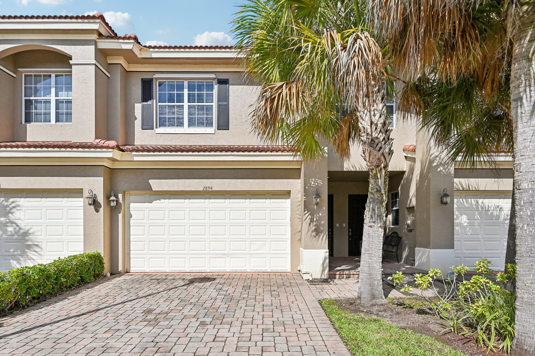 Stucco exterior with a tile roof, featuring an attached garage with a panel door, and a paver driveway
