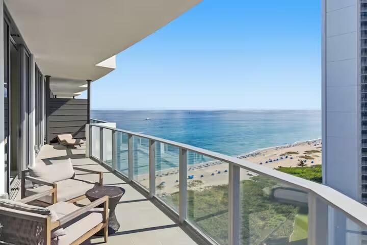 Expansive balcony featuring glass railings, direct ocean frontage, and a sandy beach